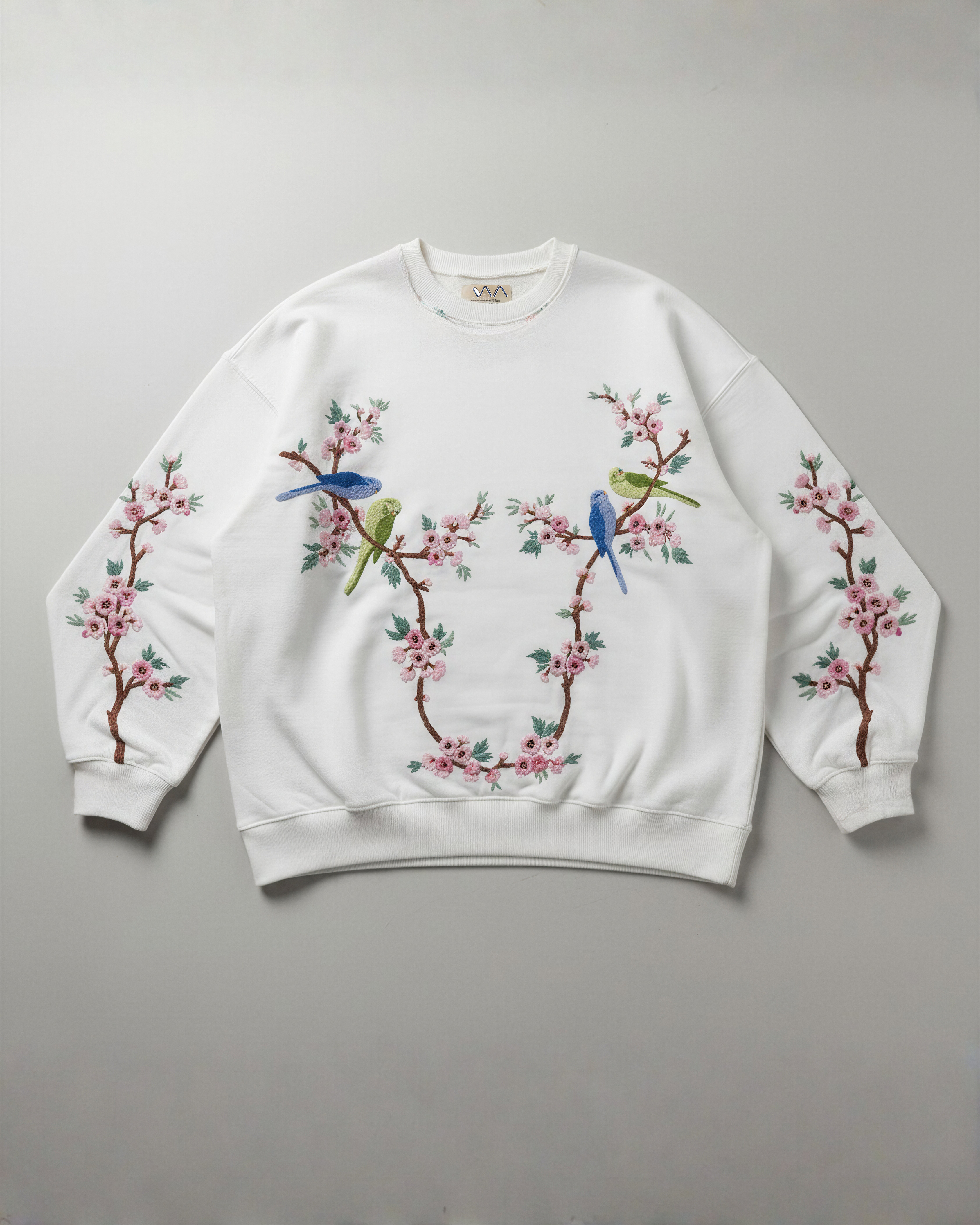 White sweatshirt with floral and bird designs han dembroidery on a gray background