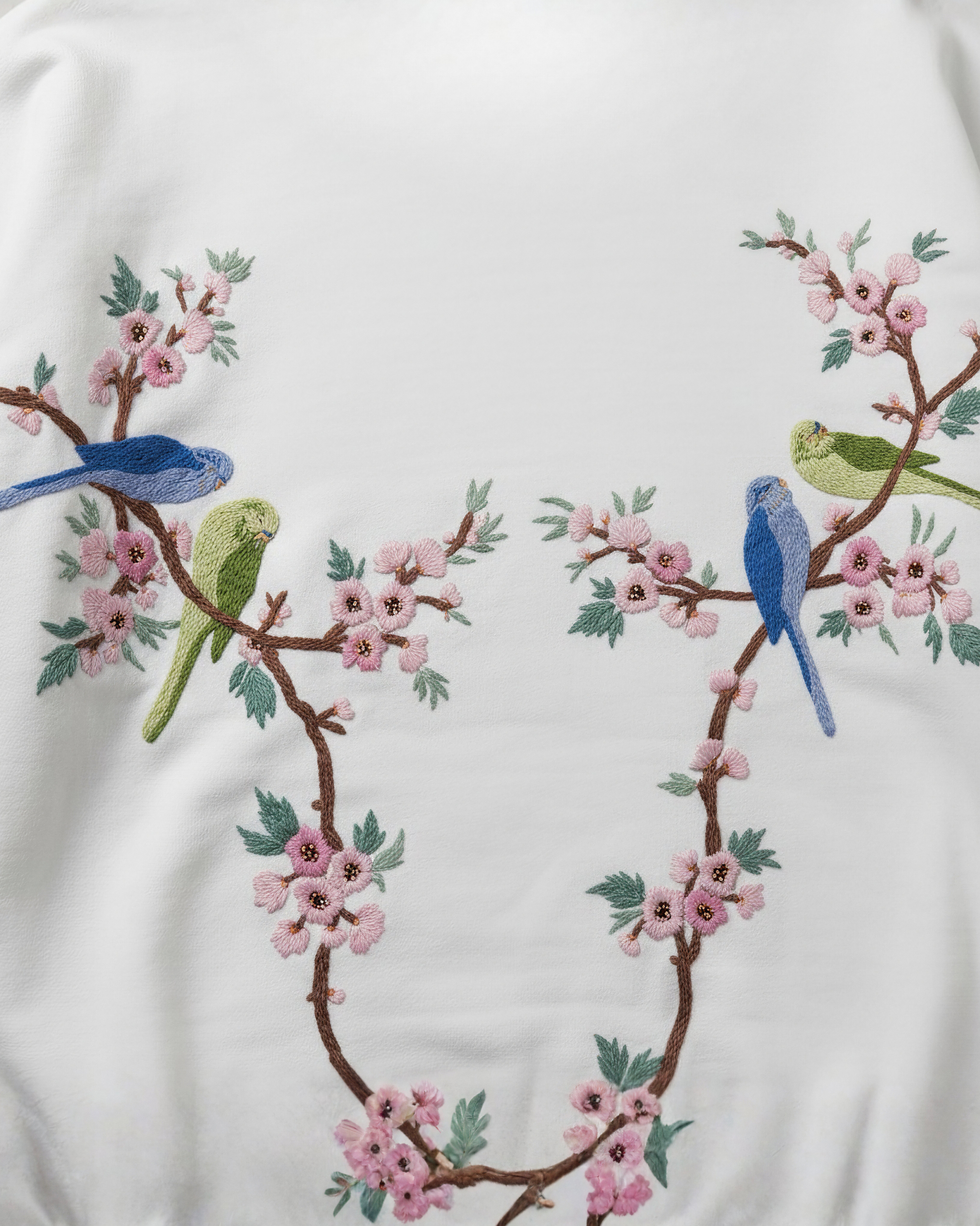 Embroidered design of birds and cherry blossoms on a white fabric