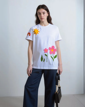 Model wearing oversized black t-shirt with multi-color floral embroidery across the chest, paired with light-wash denim.