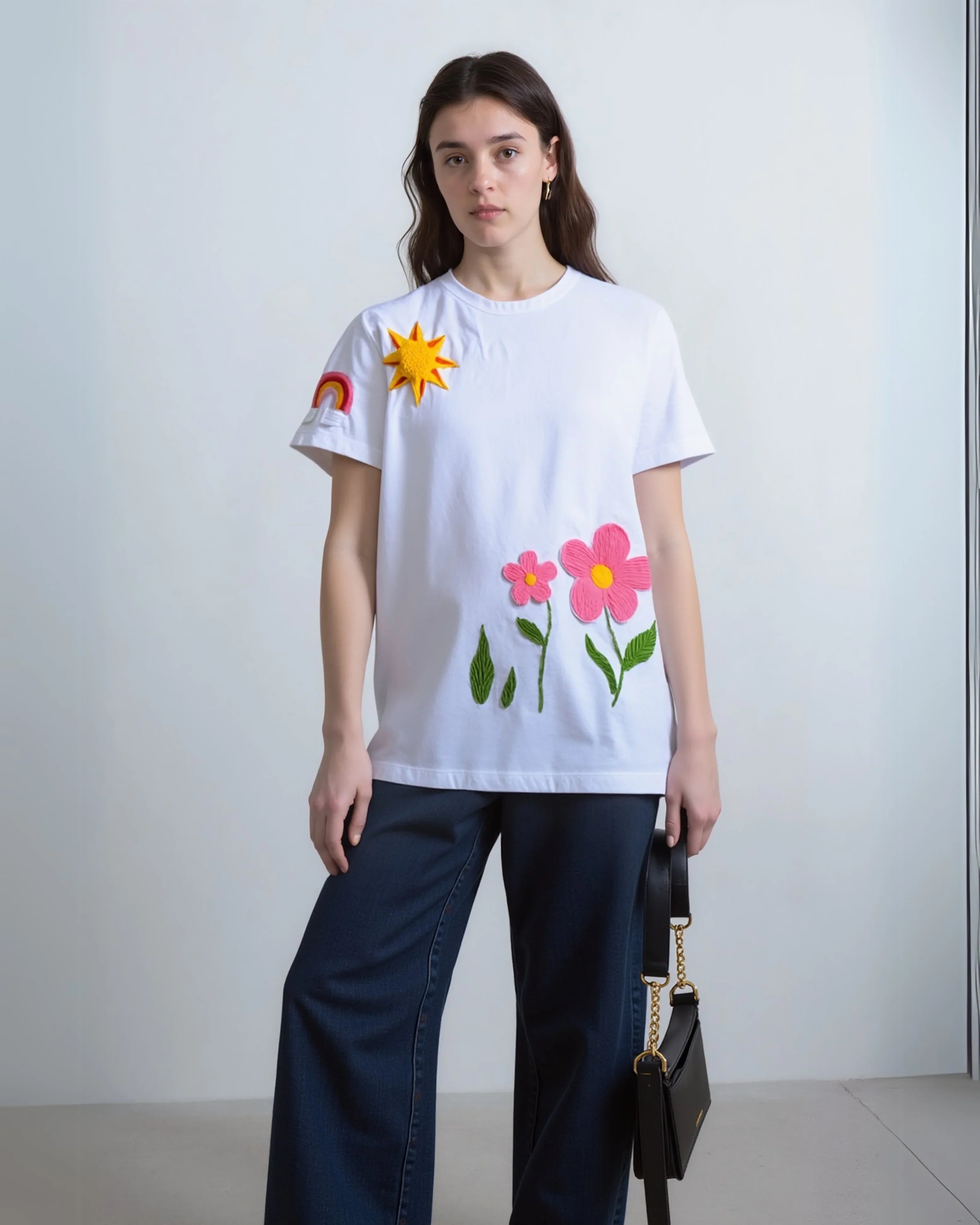 Model wearing oversized black t-shirt with multi-color floral embroidery across the chest, paired with light-wash denim.