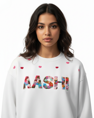 Woman wearing a white sweatshirt with colorful letters spelling 'MASHI' custom name hand embroidered on a plain background