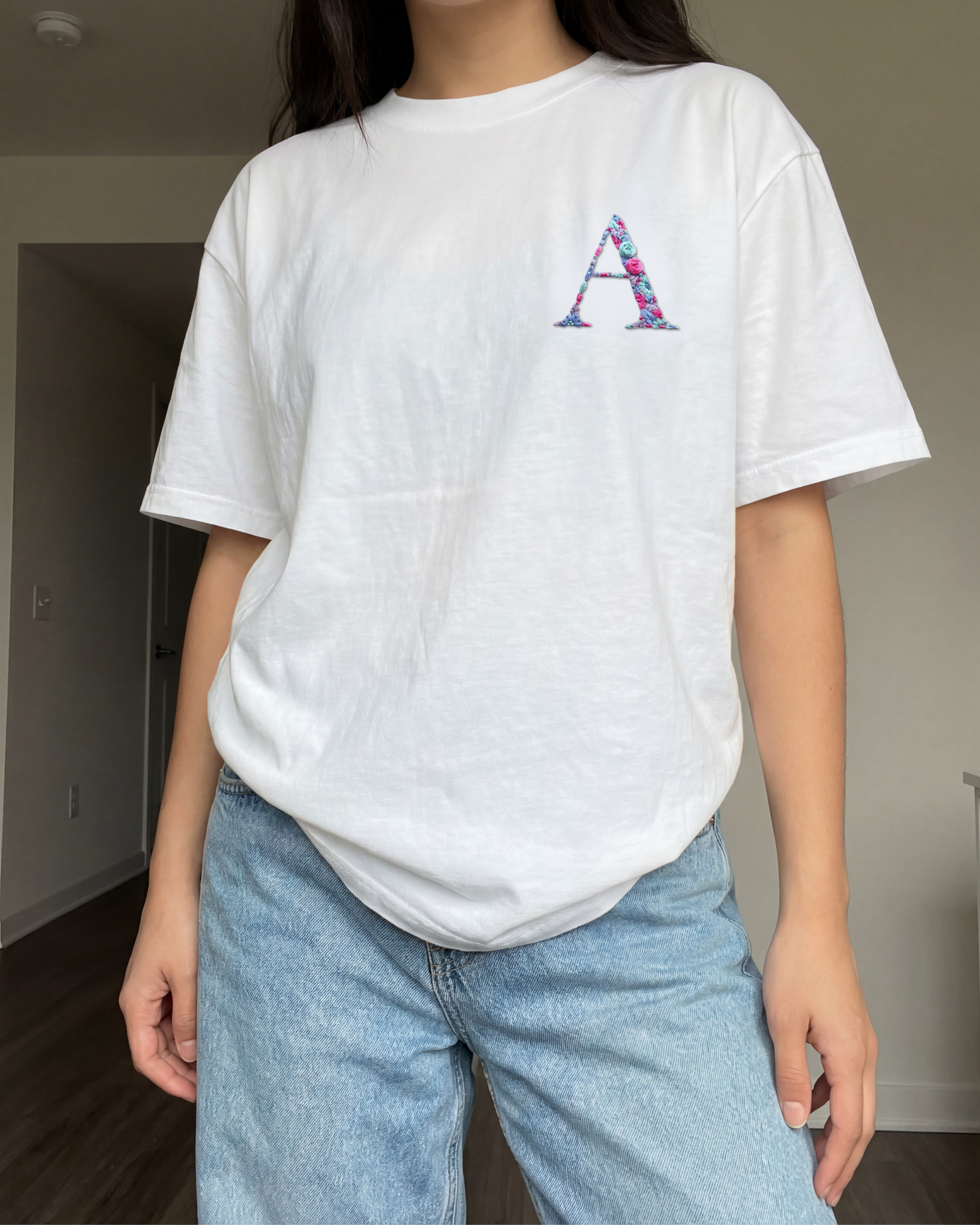 Person wearing a white t-shirt with a colorful letter 'A' embroidered and light blue jeans indoors.