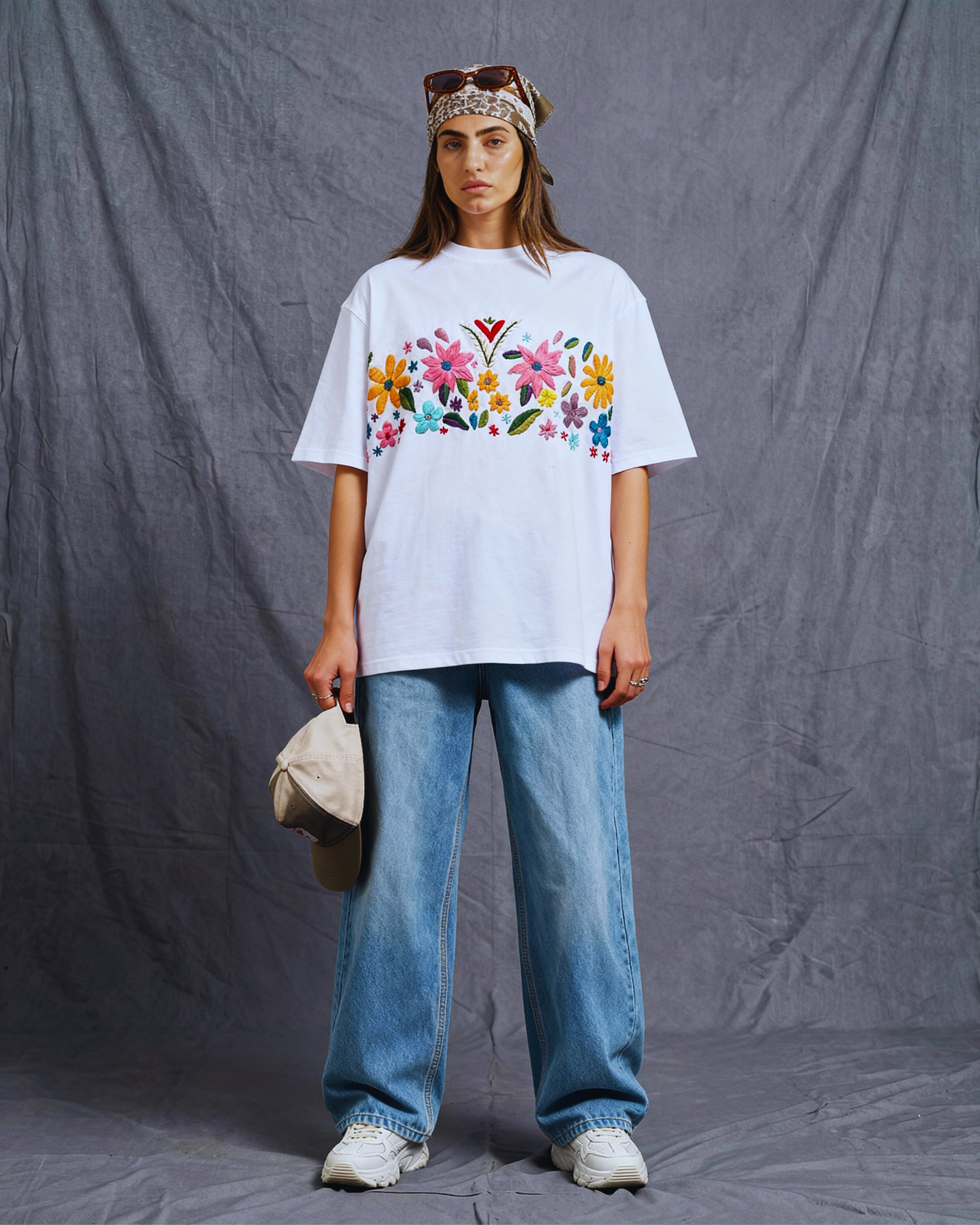 Person wearing a white t-shirt with colorful floral embroidered and blue jeans against a gray background