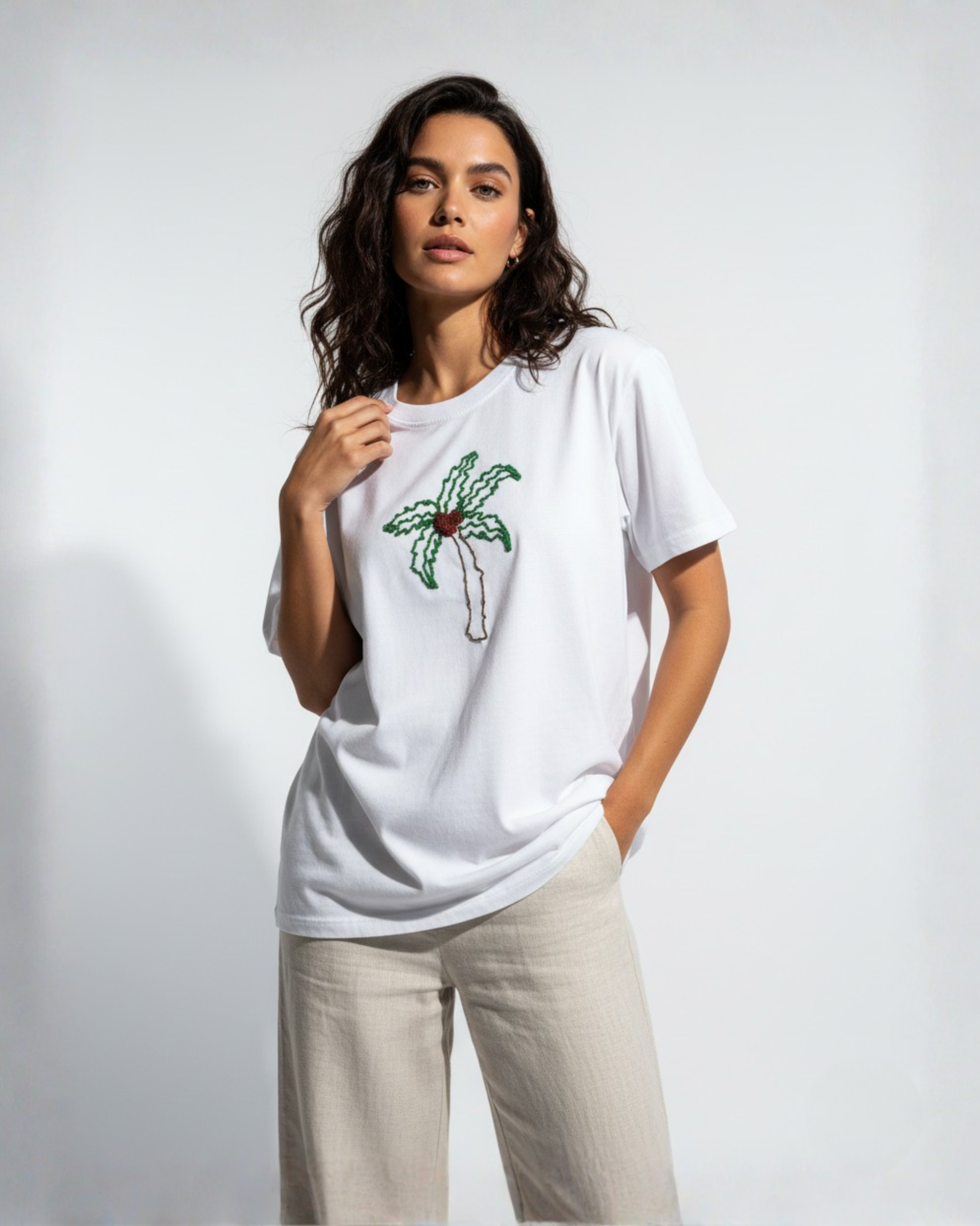 Woman wearing a white t-shirt with a palm tree bead embroidered design on a plain background