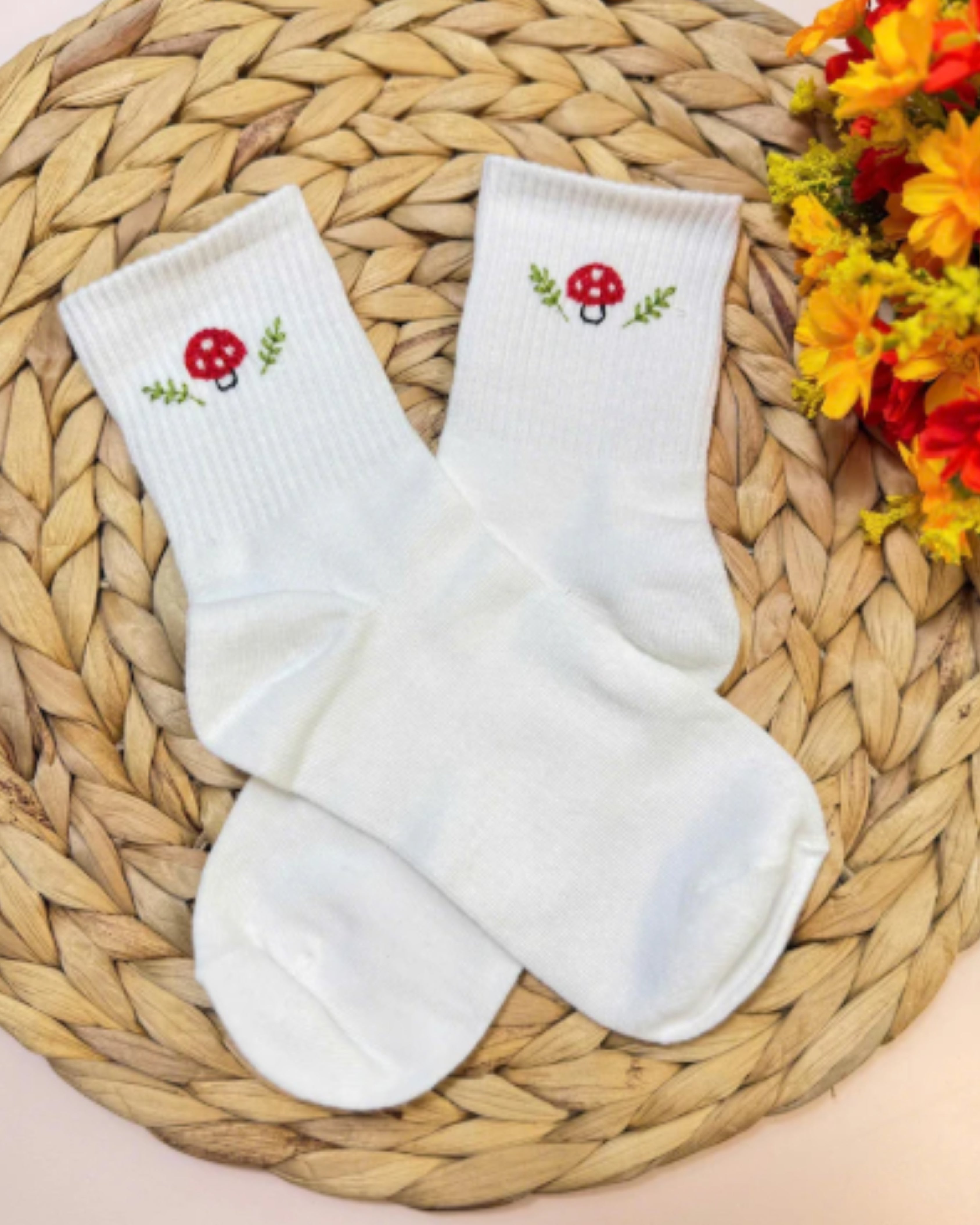 White socks with mushroom embroidered design on a woven mat with flowers in the background