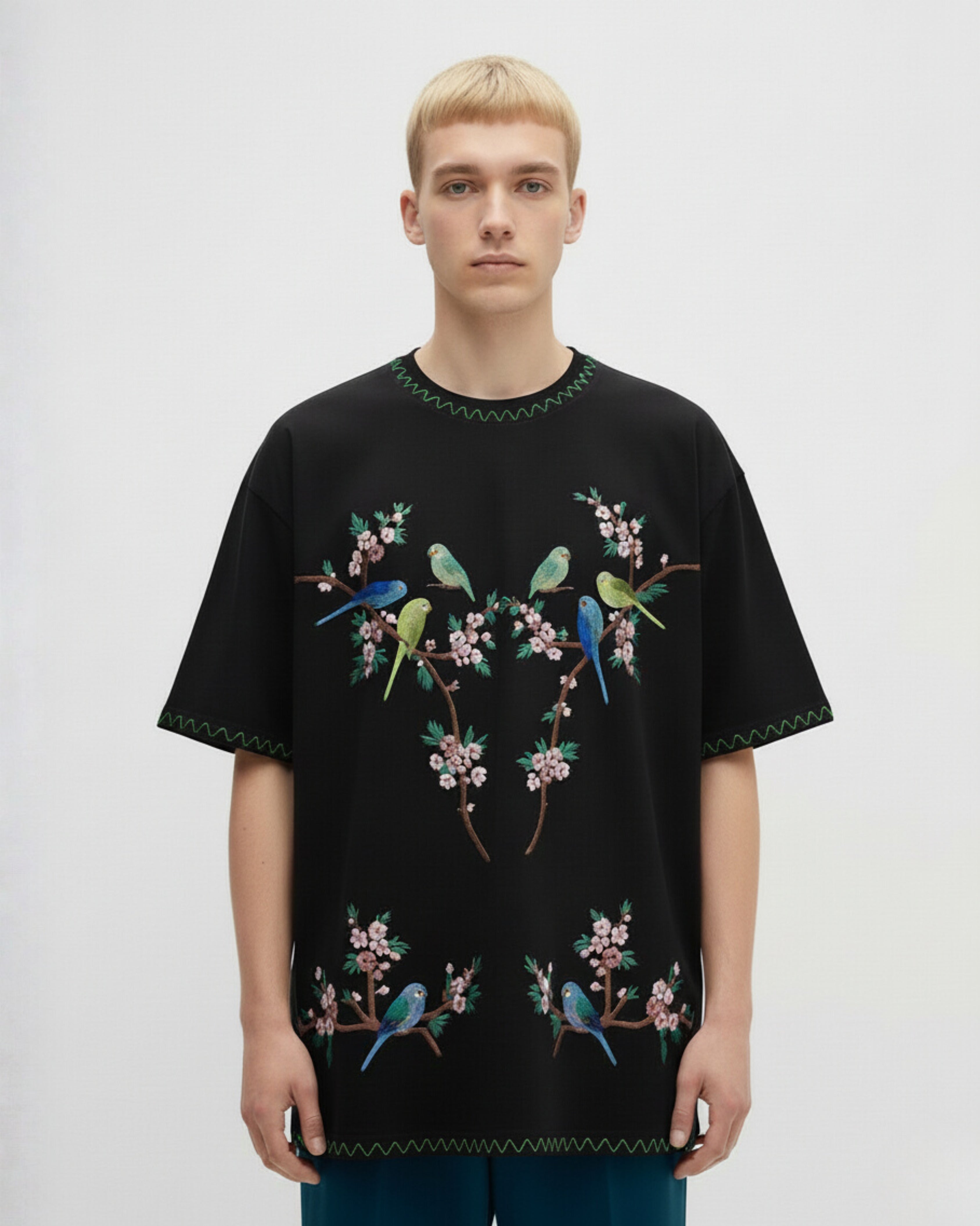 Person wearing a black t-shirt with colorful bird and floral embroidery on a plain background