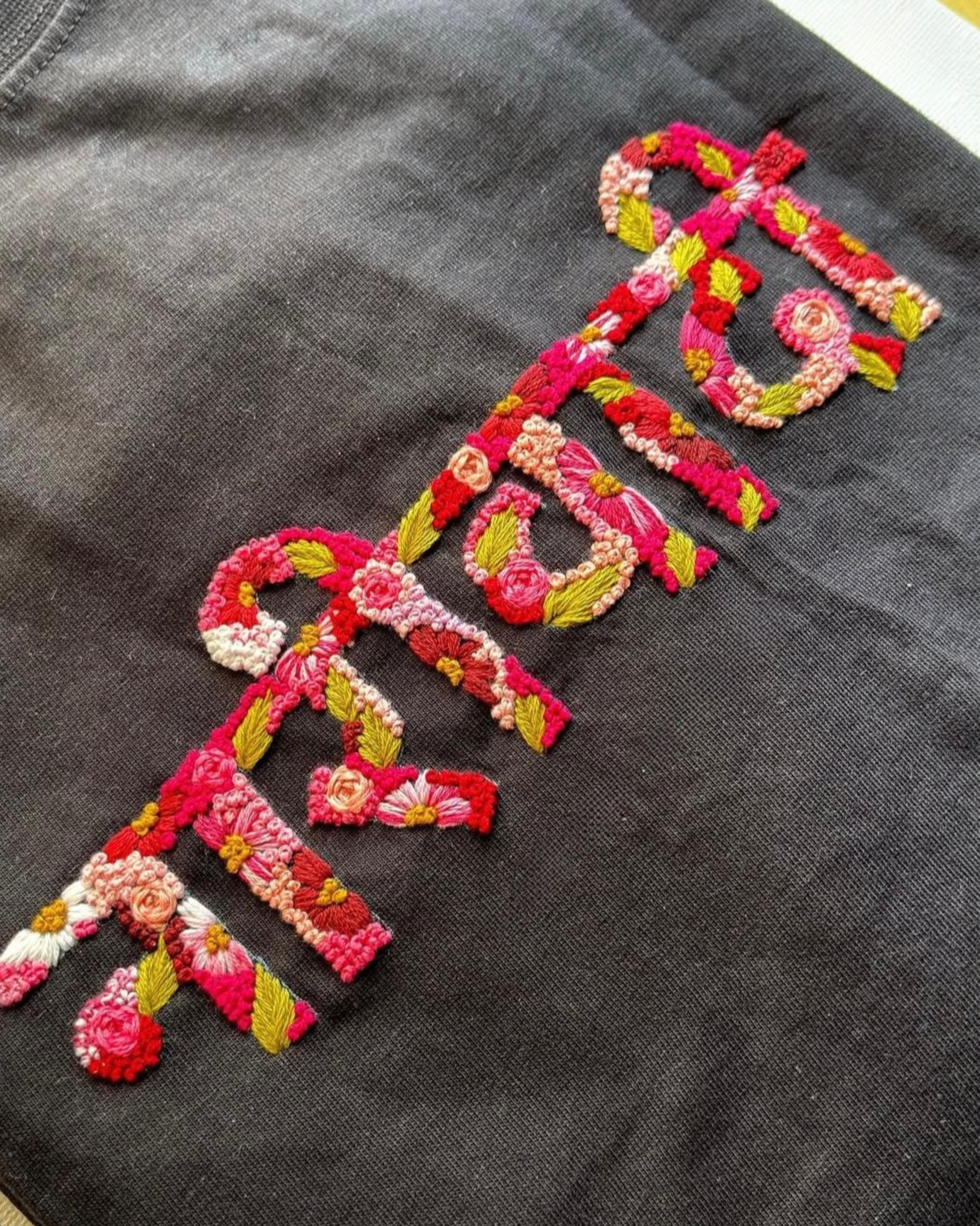 Flatlay of black oversized custom t-shirt with hand-embroidered name in white thread, designed for gifting and personalization.