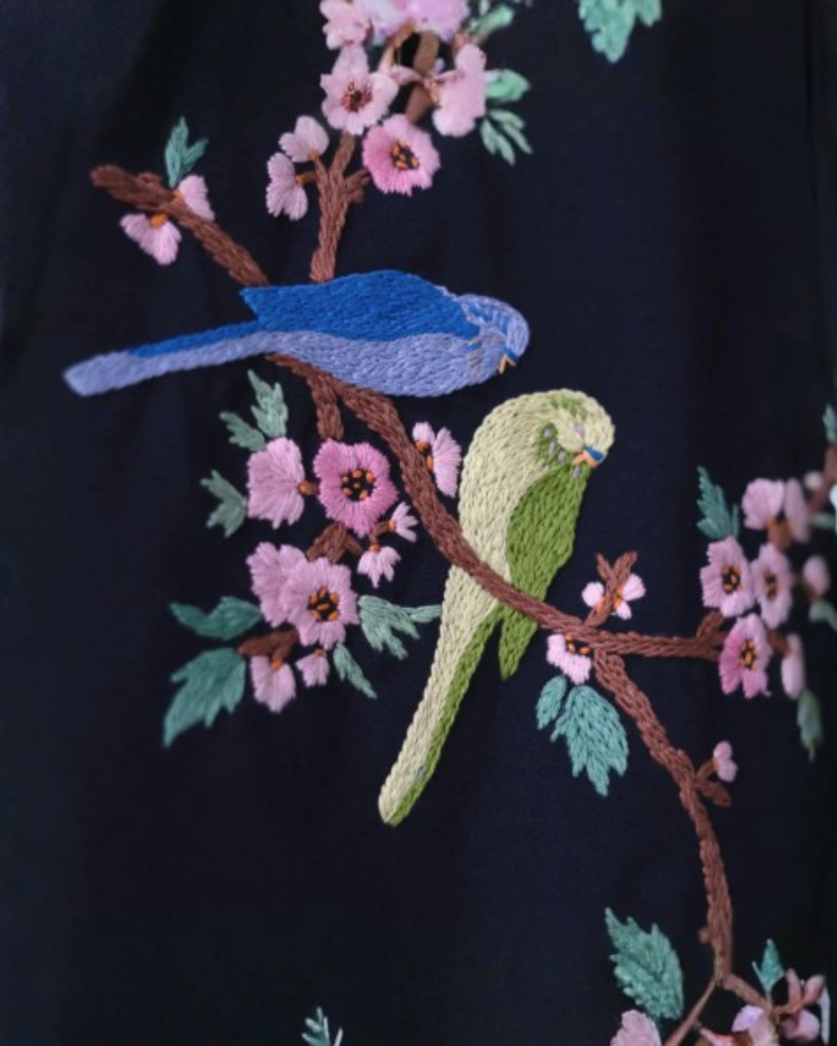 Embroidered design of birds and flowers on a dark fabric background