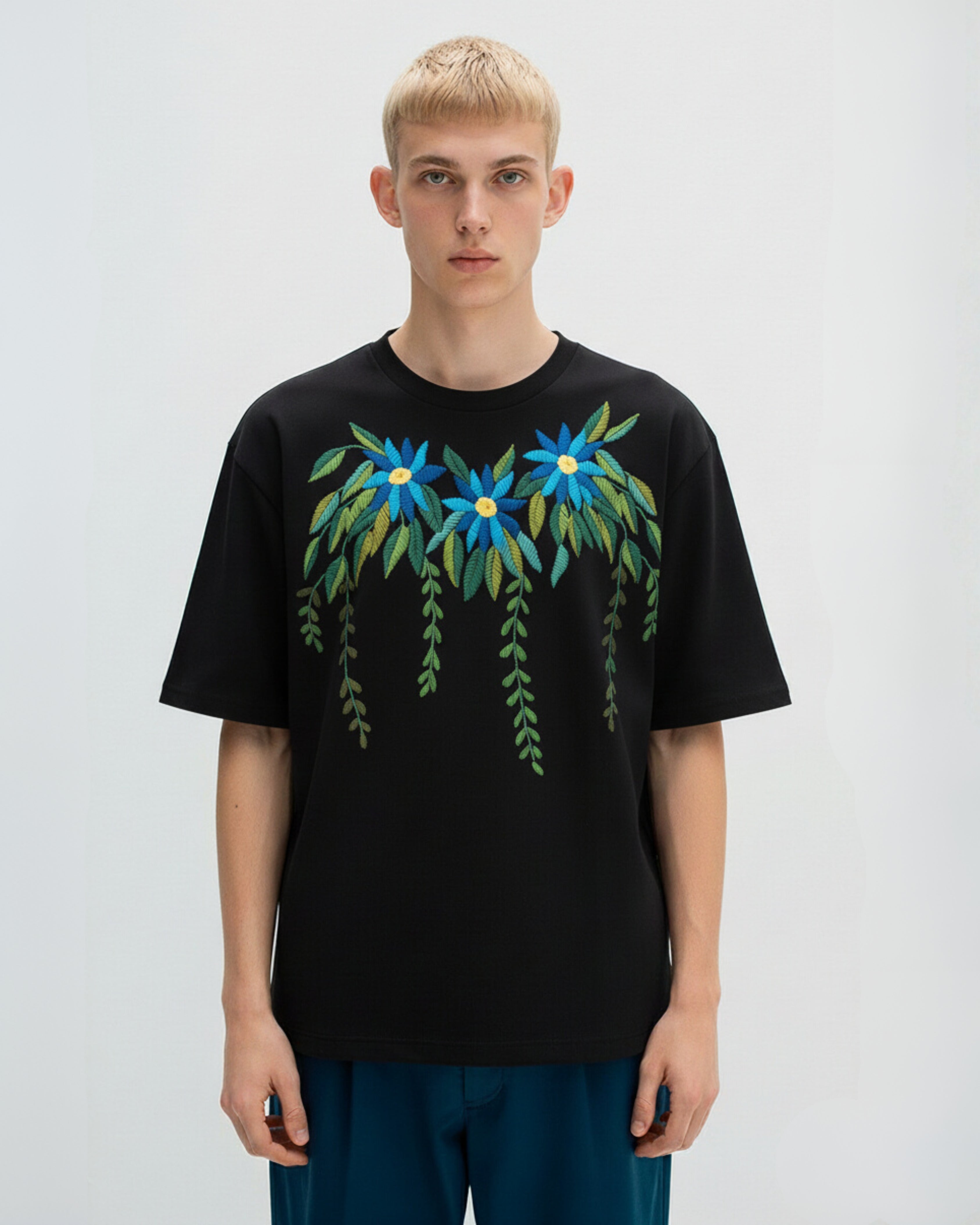 Person wearing a black t-shirt with hand embroidered floral design on a plain background