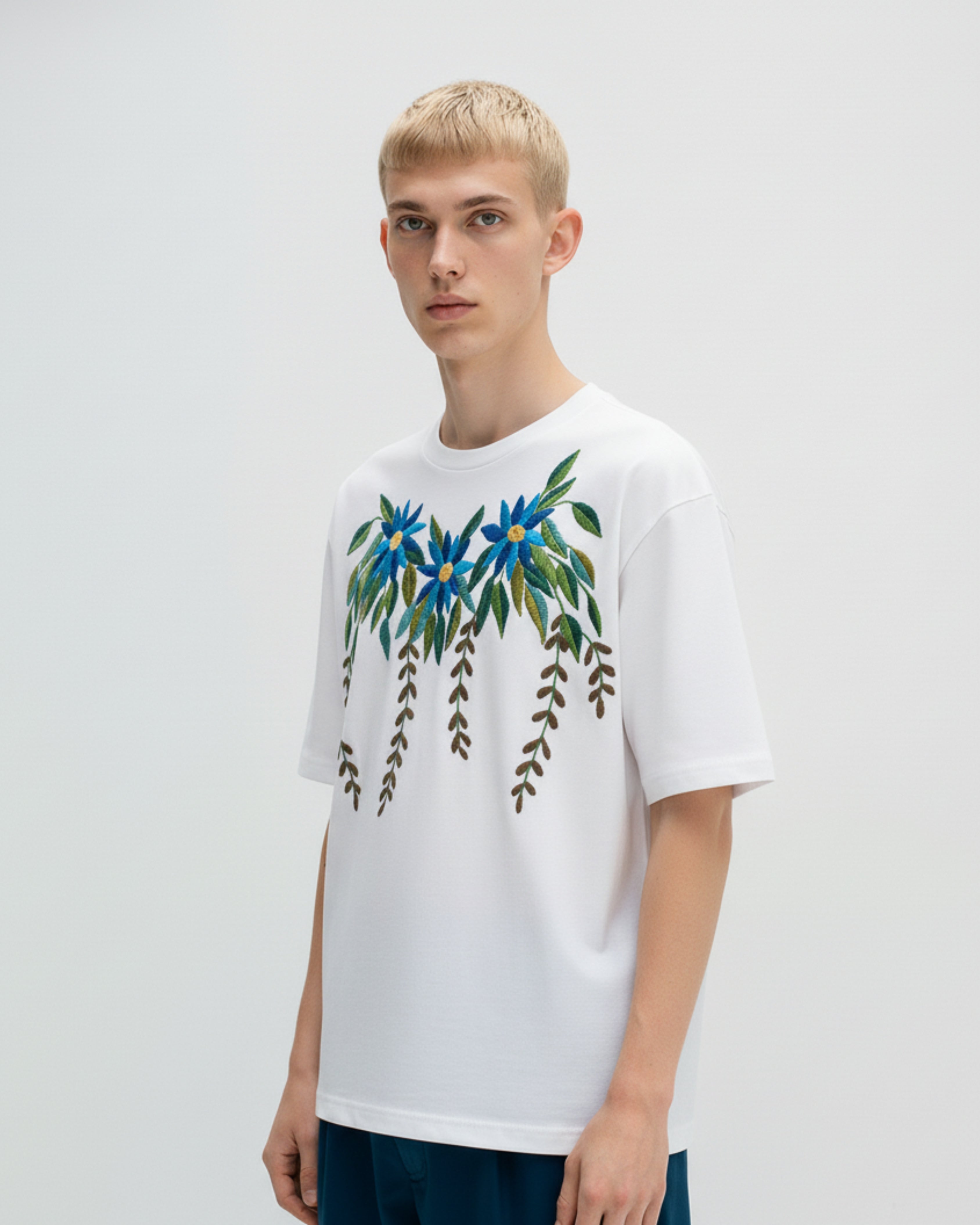 Person wearing a white t-shirt with floral hand embroidered design on a plain background
