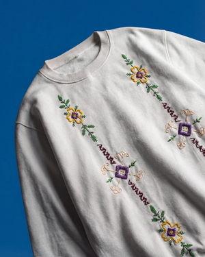 White sweatshirt with colorful floral embroidery on a blue background
