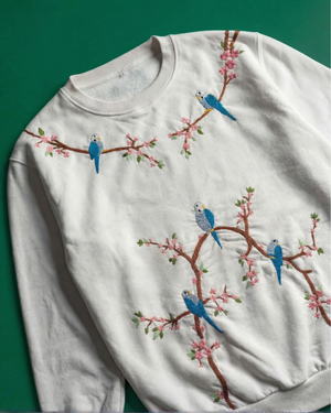 White sweatshirt with embroidered blue birds and pink flowers on a green background