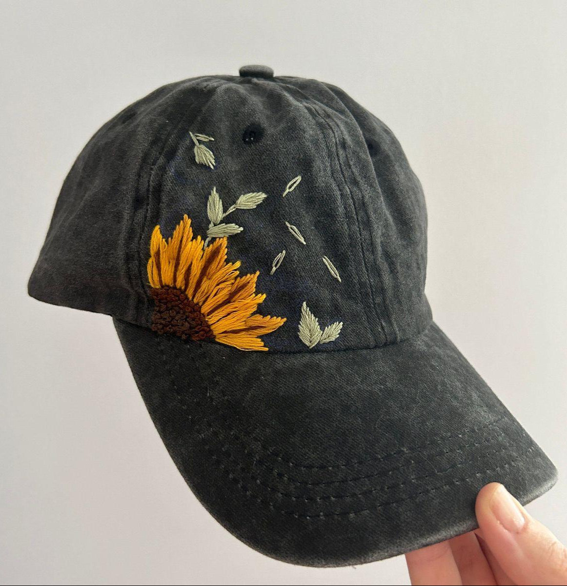 Black baseball cap with sunflower embroidery on a light gray background