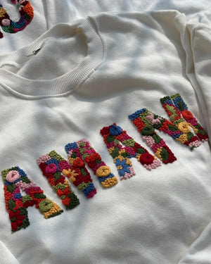 Personalised sweatshirt with hand-stitched name folded neatly on a neutral background with a gift card beside it