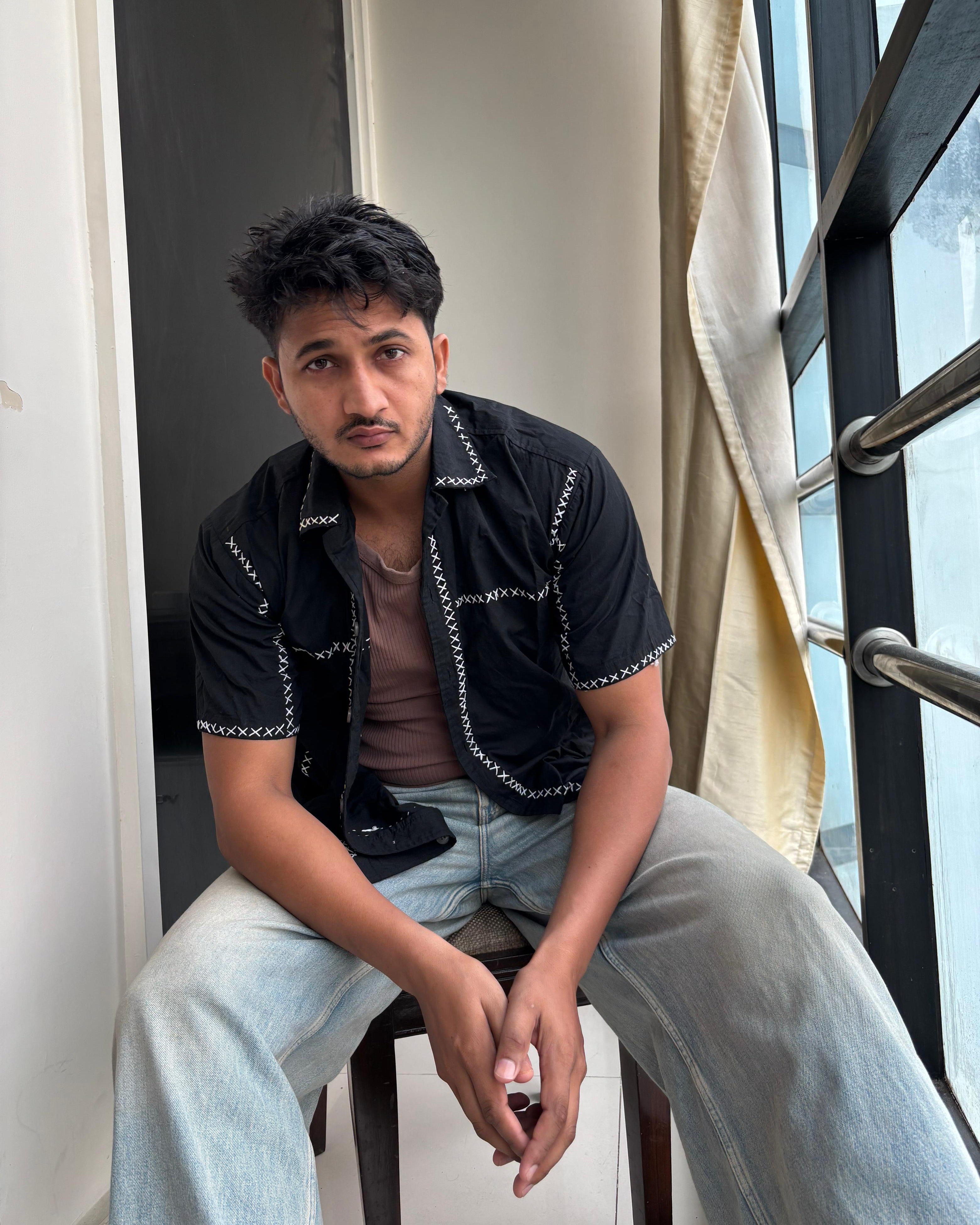 Person sitting on a chair indoors wearing embroidered shirt
