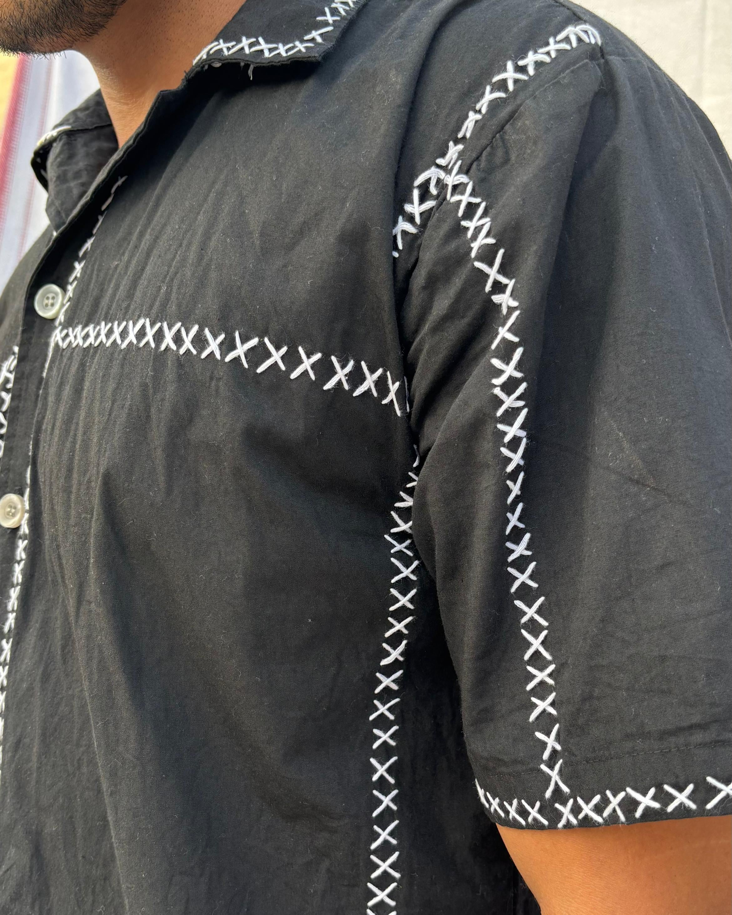 Black shirt with white embroidery stitching details on the collar and sleeves.