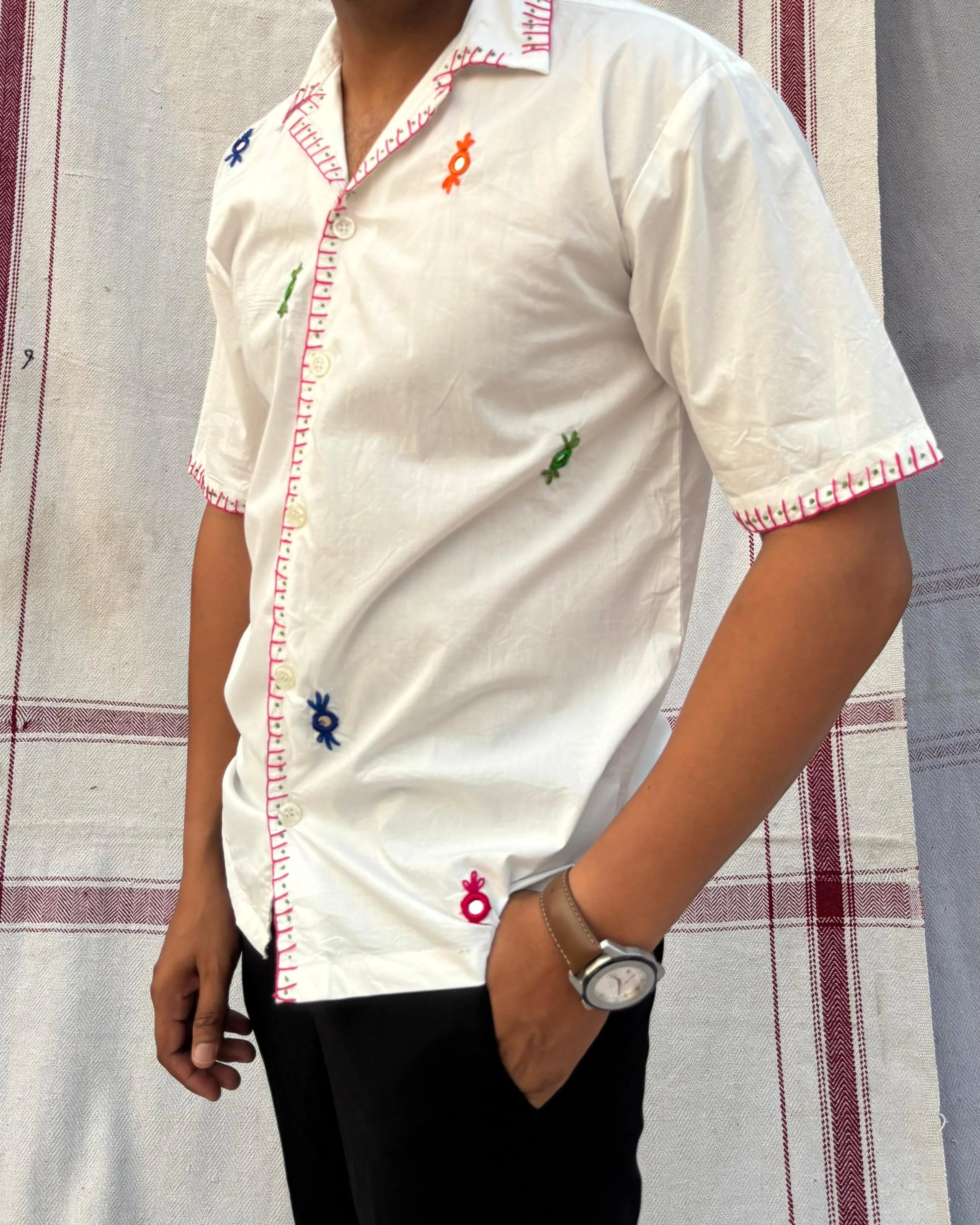 Person wearing a white shirt with red and blue accents embroidered against a patterned background.