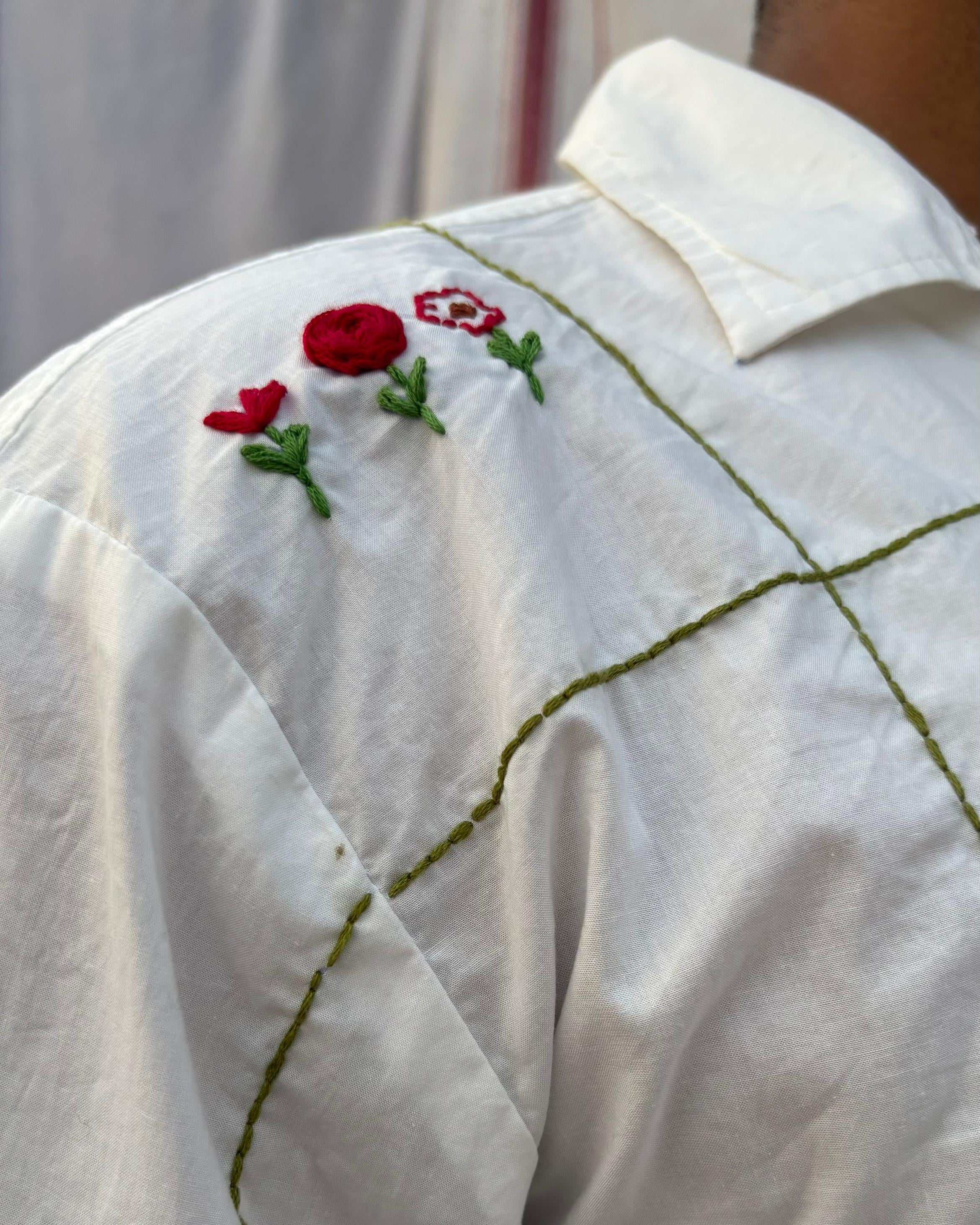 White shirt with red floral embroidery on a hanger.