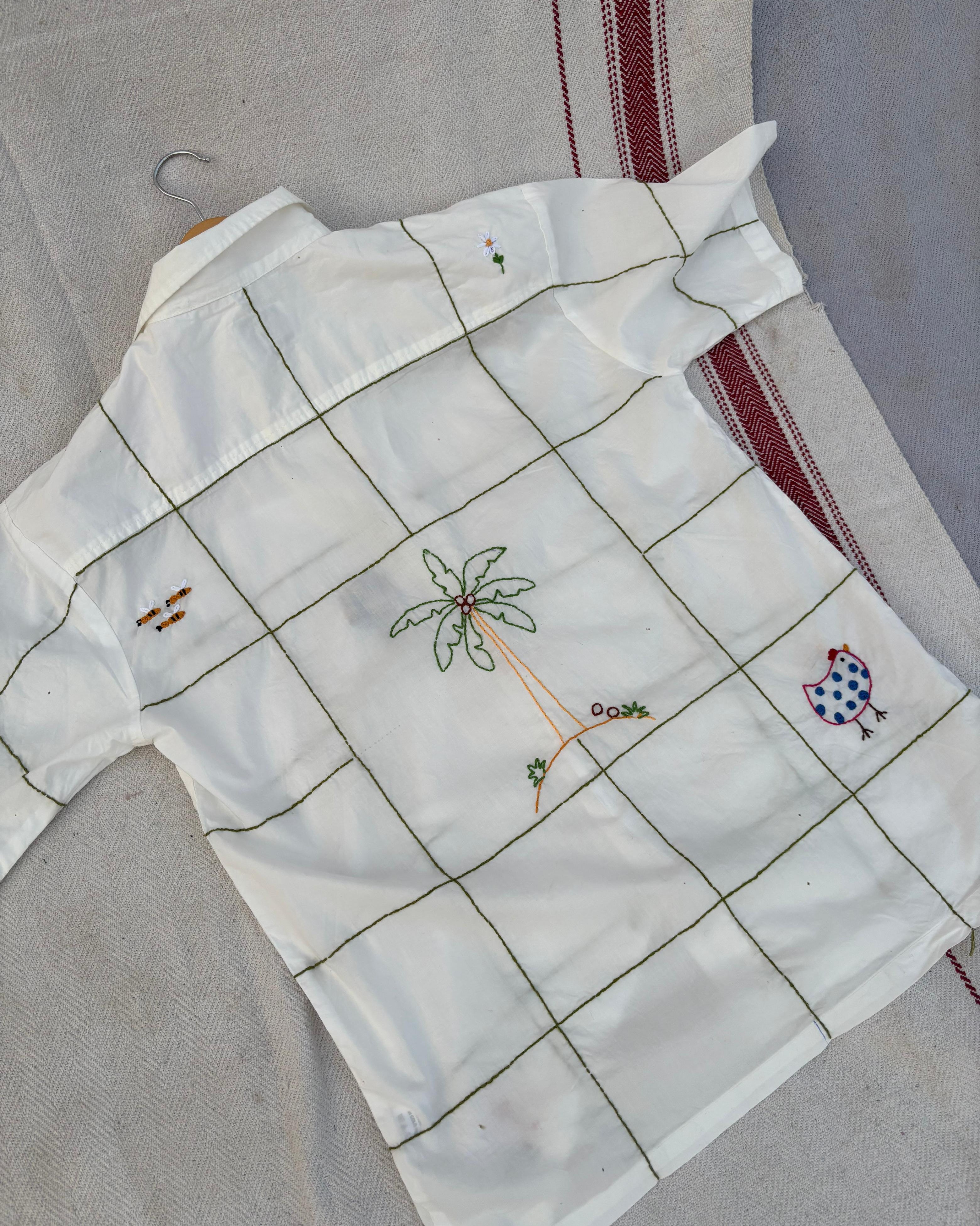 White shirt with grid pattern and embroidered designs on a textured surface