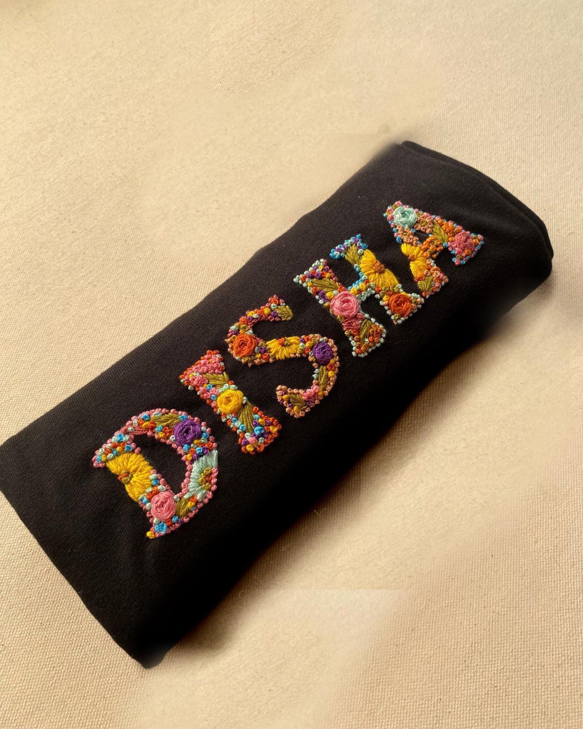 Black pouch with colorful embroidered custom name text on a beige surface