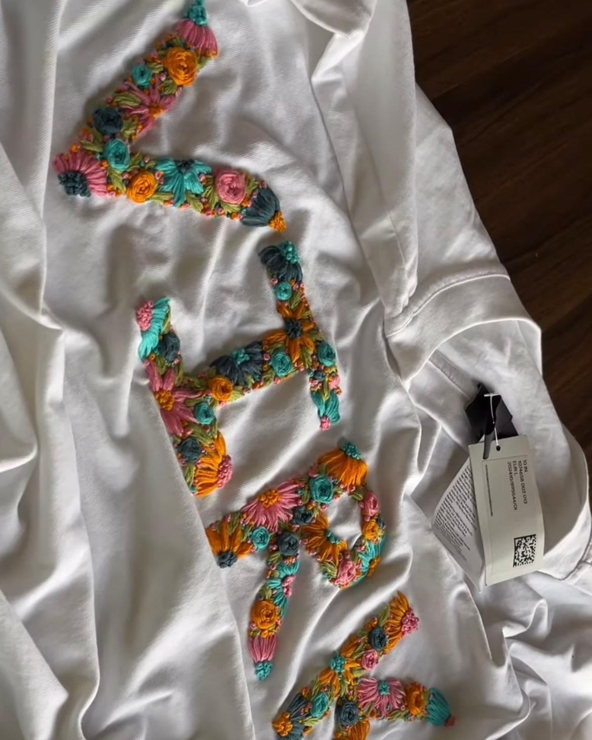 White sweatshirt with colorful floral letters on a wooden surface