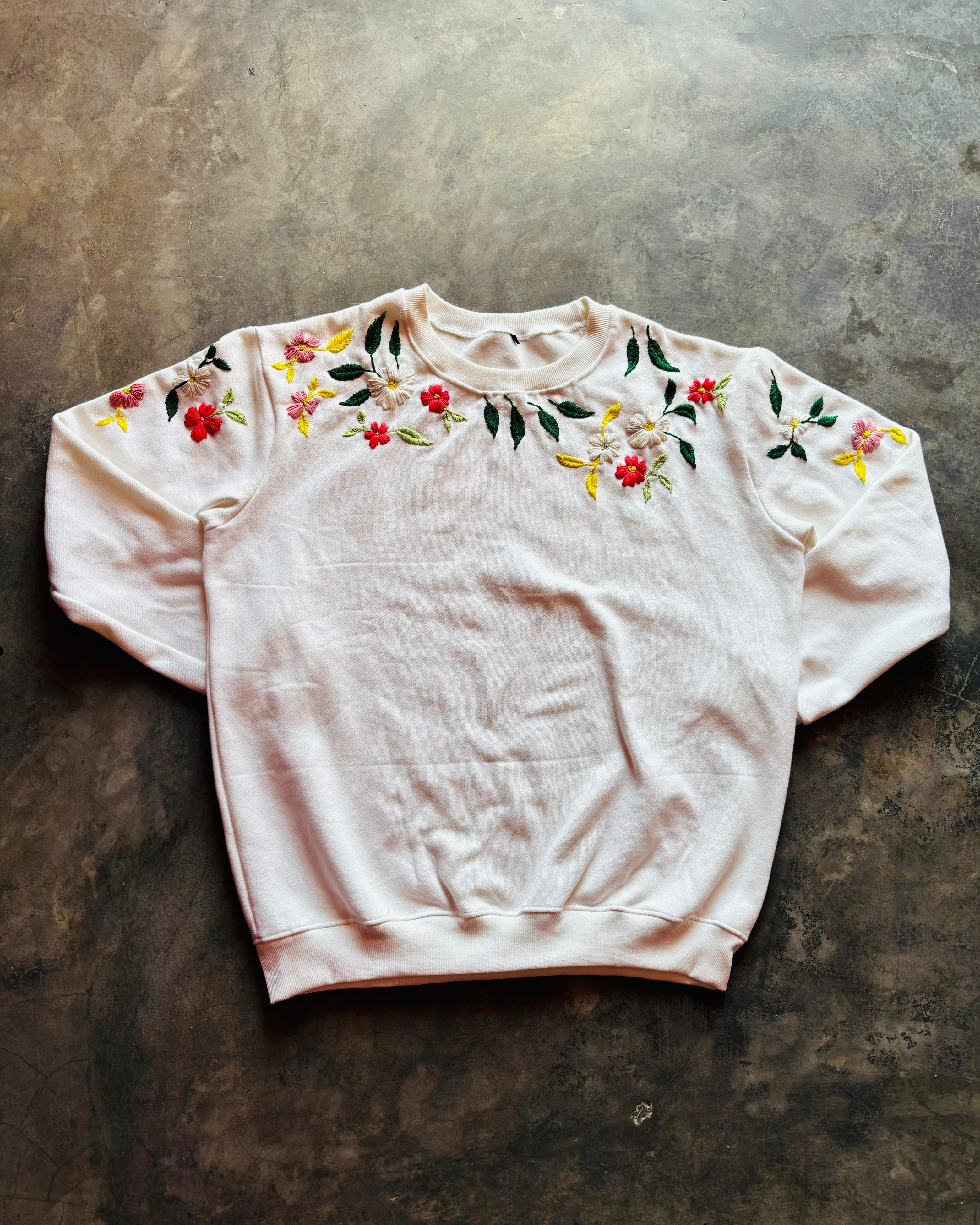 White sweatshirt with floral embroidery on a textured surface