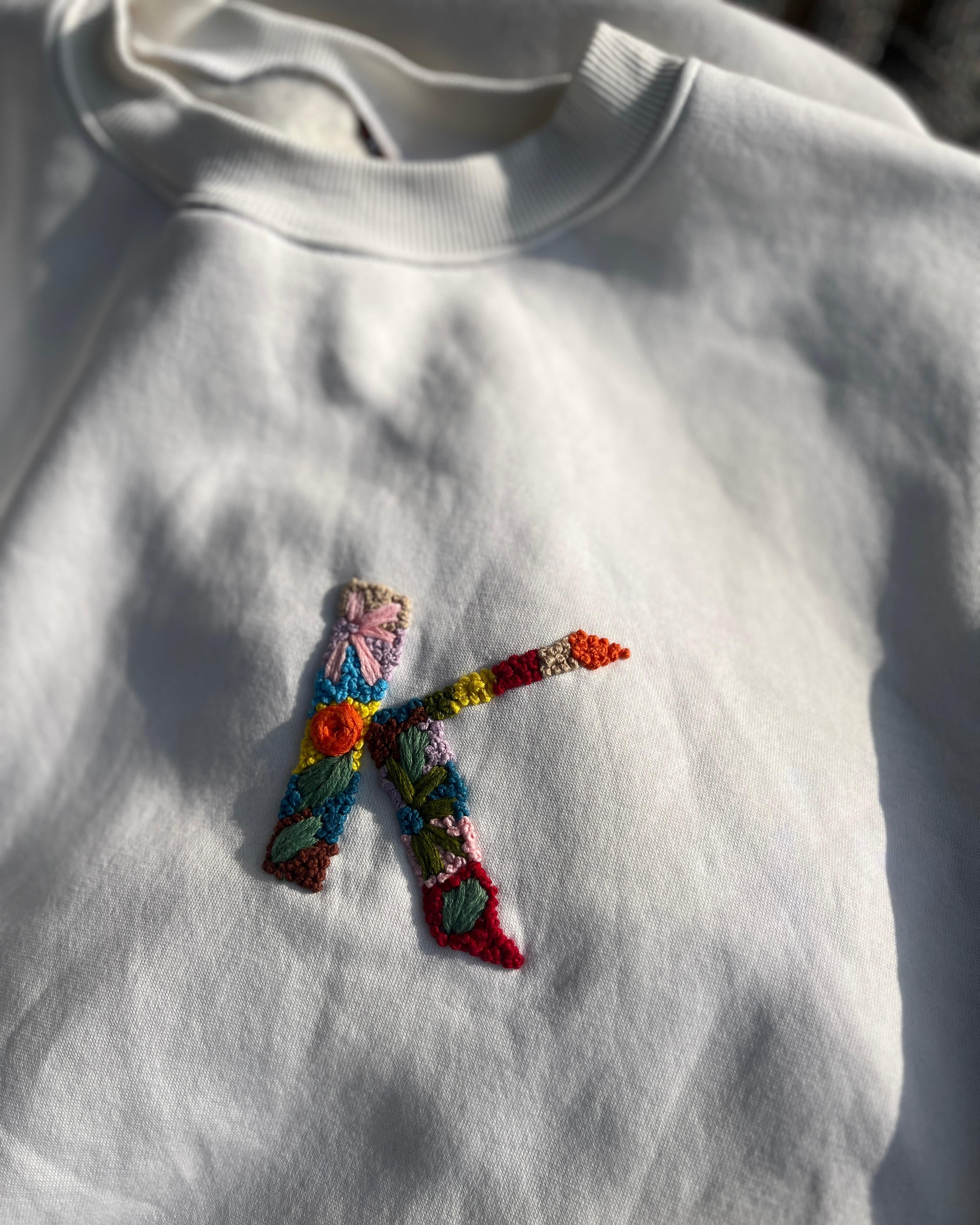 Close-up of embroidered initials on chest of cotton sweatshirt, showing fine thread detail and clean finishing.