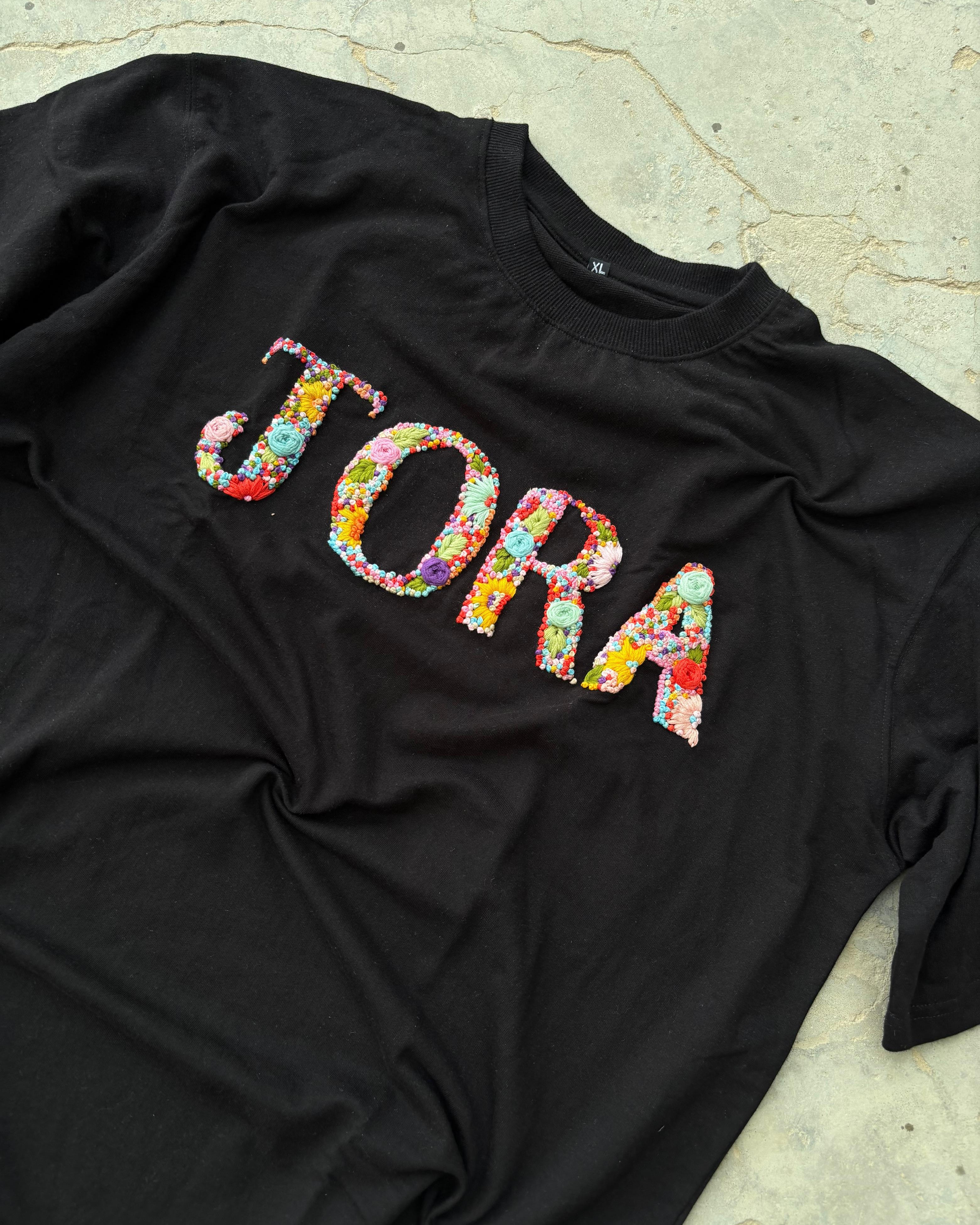 Close-up of hand-embroidered custom name on black cotton tee, showcasing fine embroidery details and premium stitching.