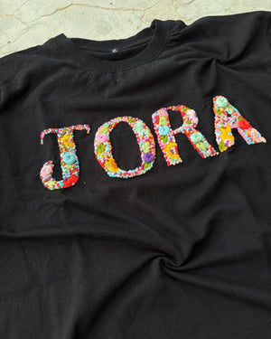 Custom t-shirt printing with name detail in multicolored thread, embroidered by skilled artisans on high-GSM cotton.