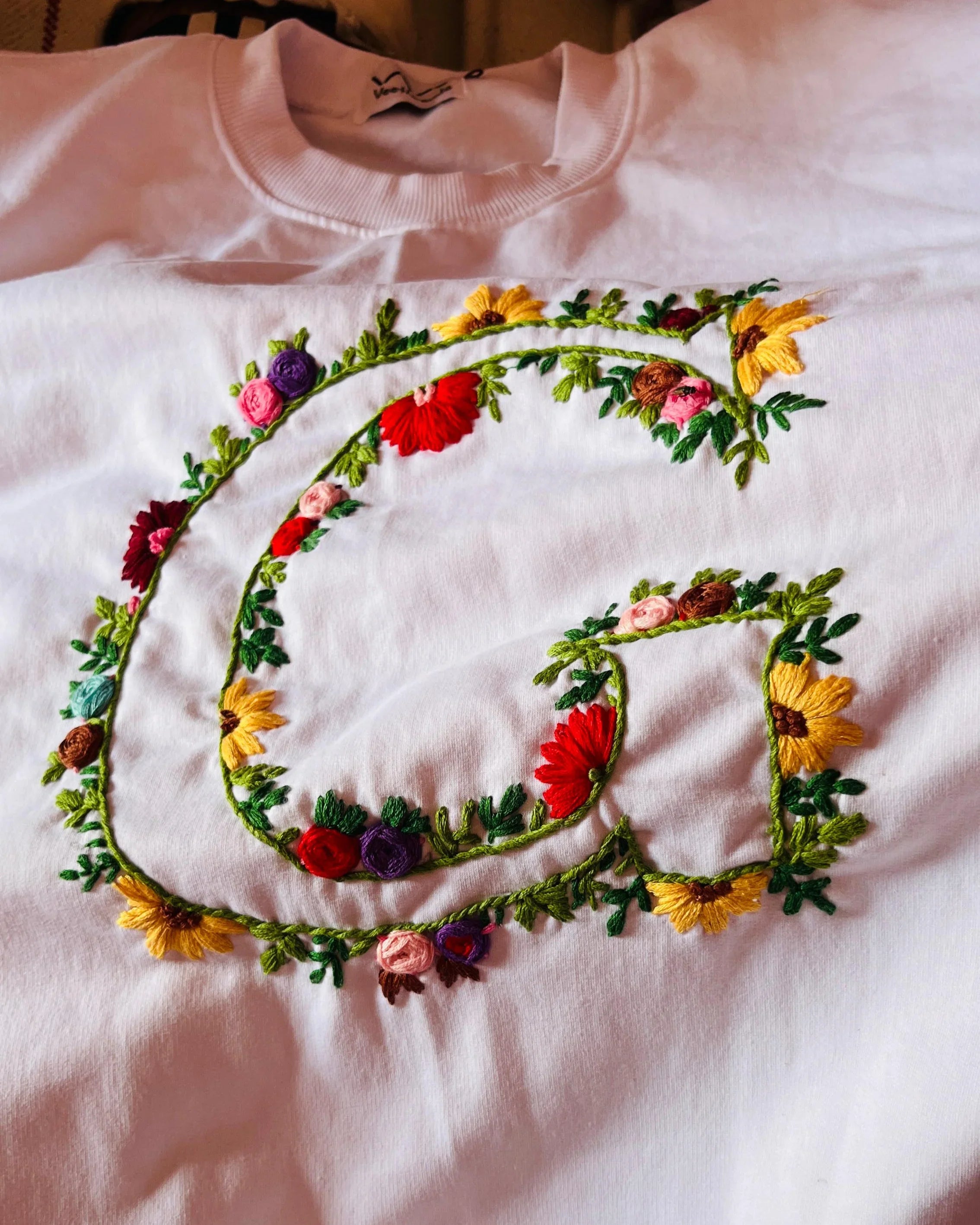 Focus on embroidery detail of hand-stitched initials on a pastel-toned custom sweatshirt.