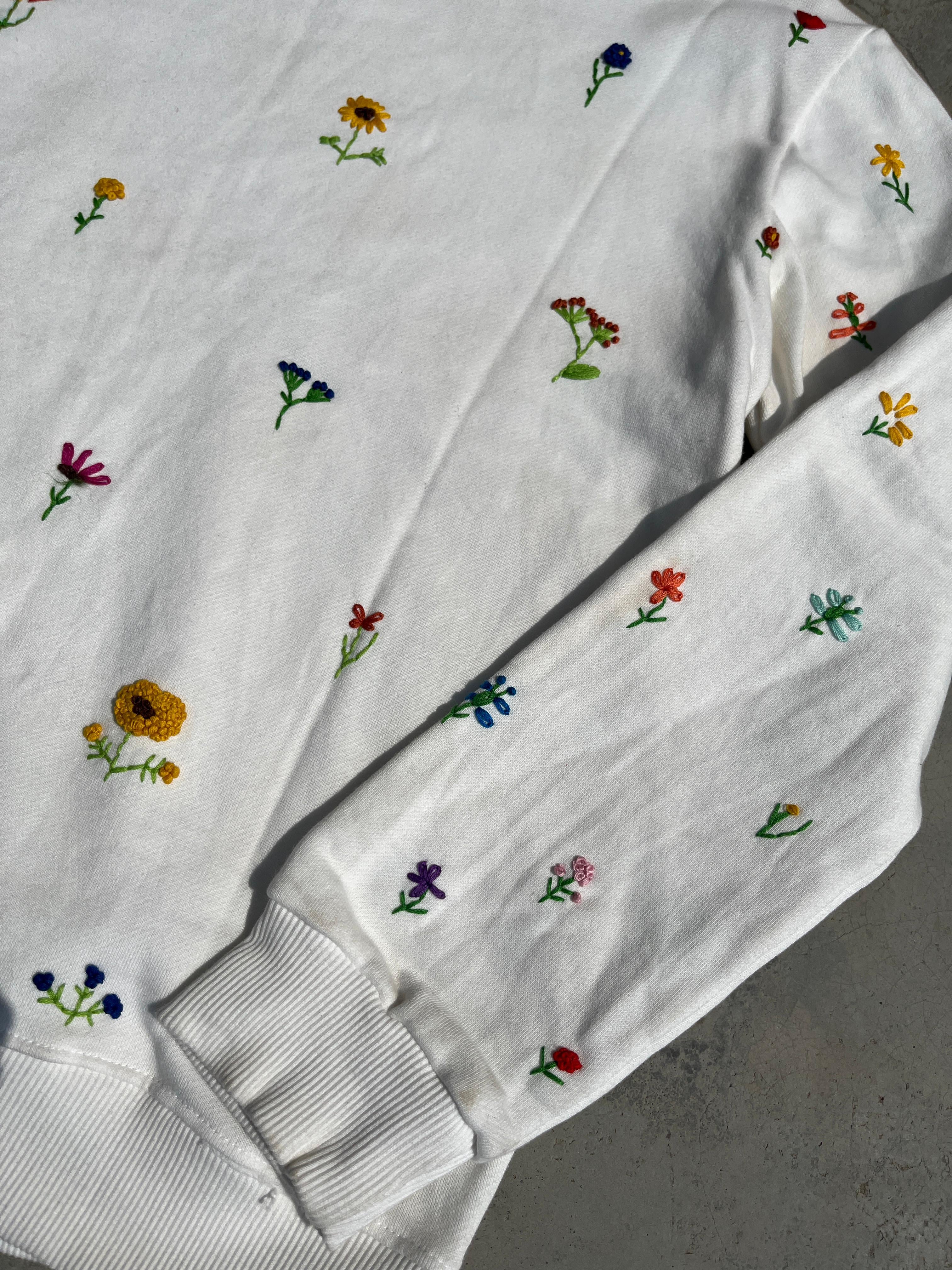 Whitehoodies with colorful embroidered flowers on a gray surface