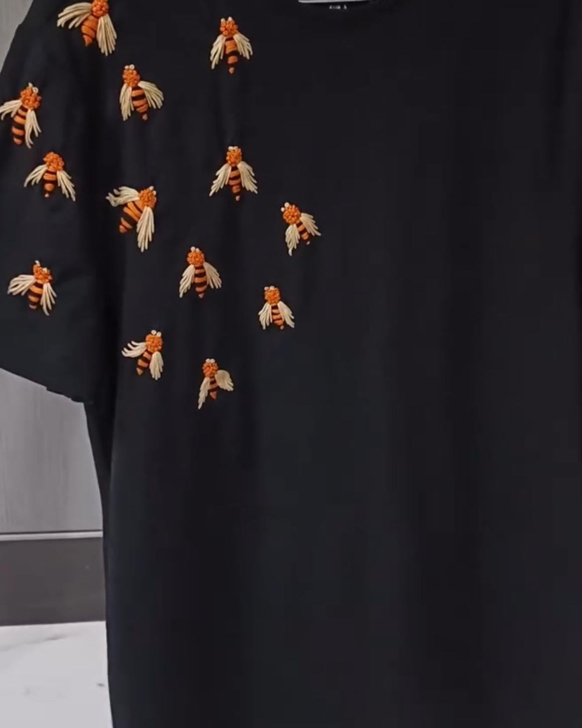 Black tshirt with embroidered bee designs on a plain background