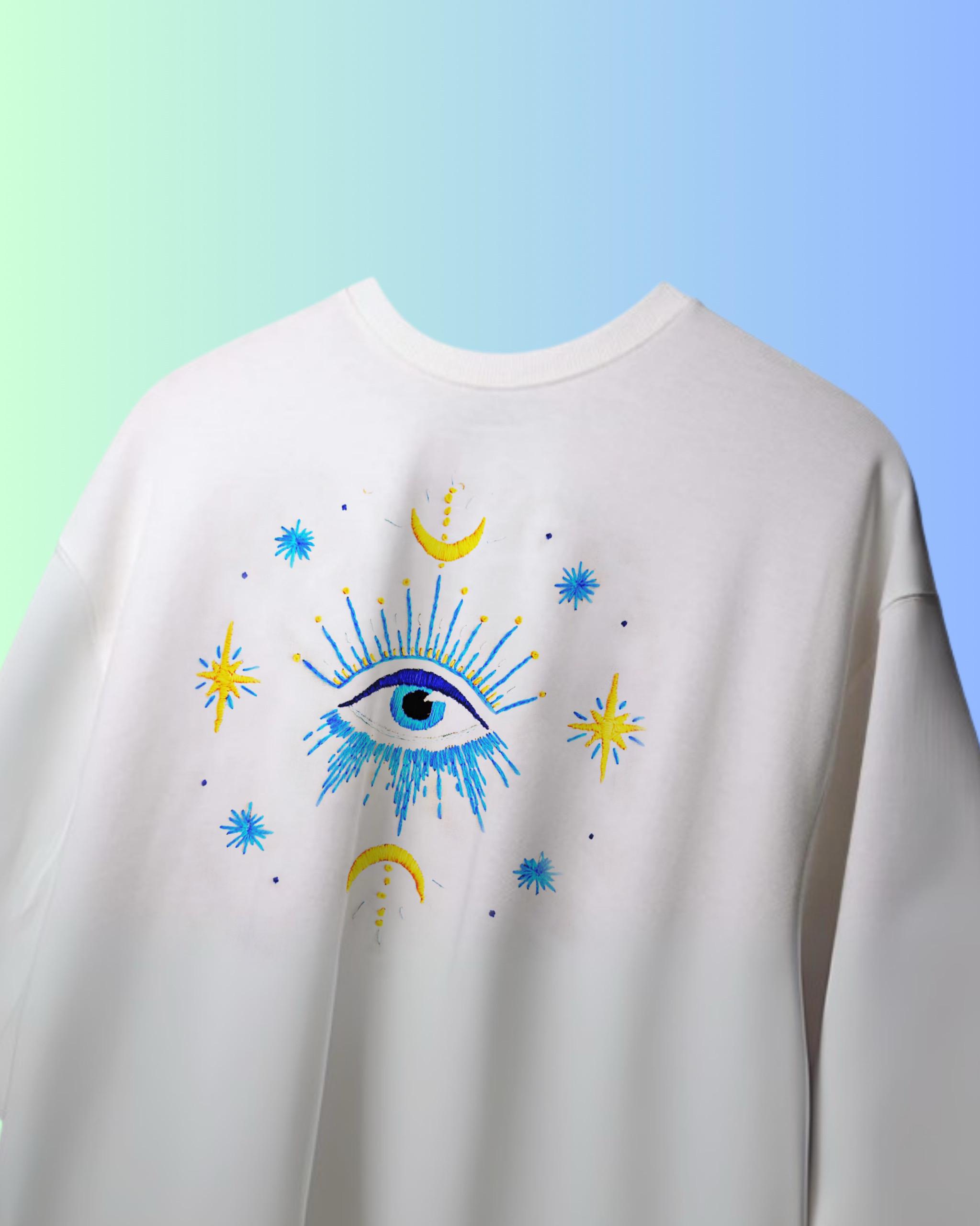 Oversized evil eye shirt featuring artisan hand embroidery for protection on a gradient background