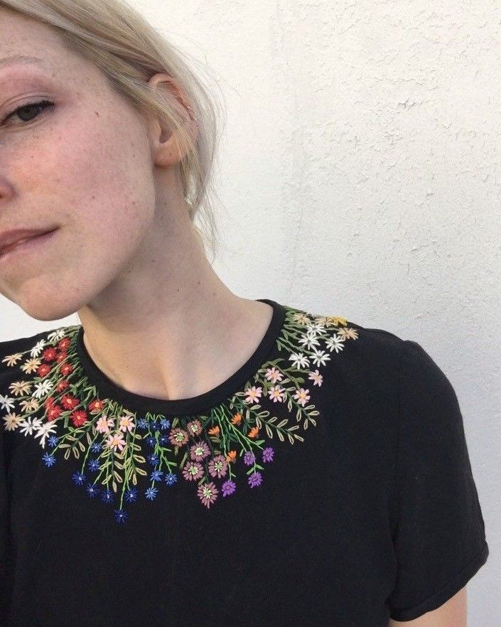 Person wearing a black shirt with colorful floral embroidery on a white background