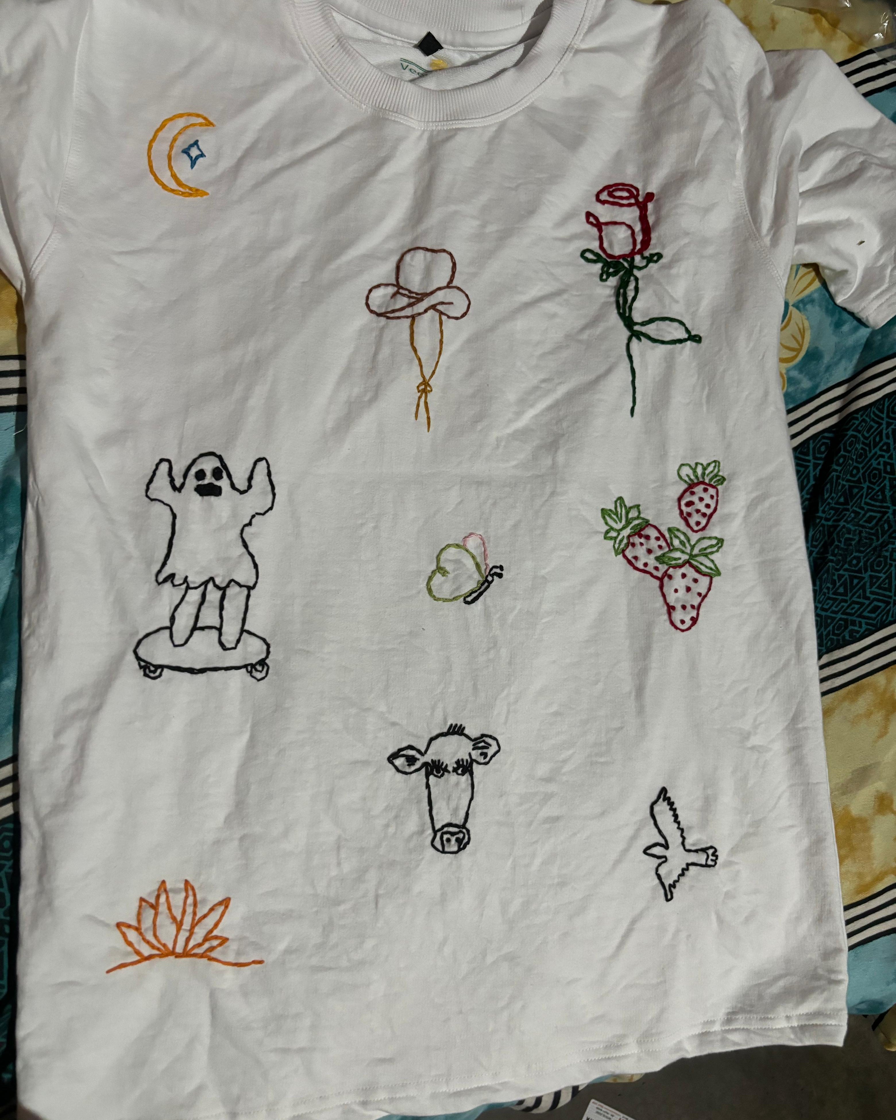 White t-shirt with various embroidered designs on a patterned surface