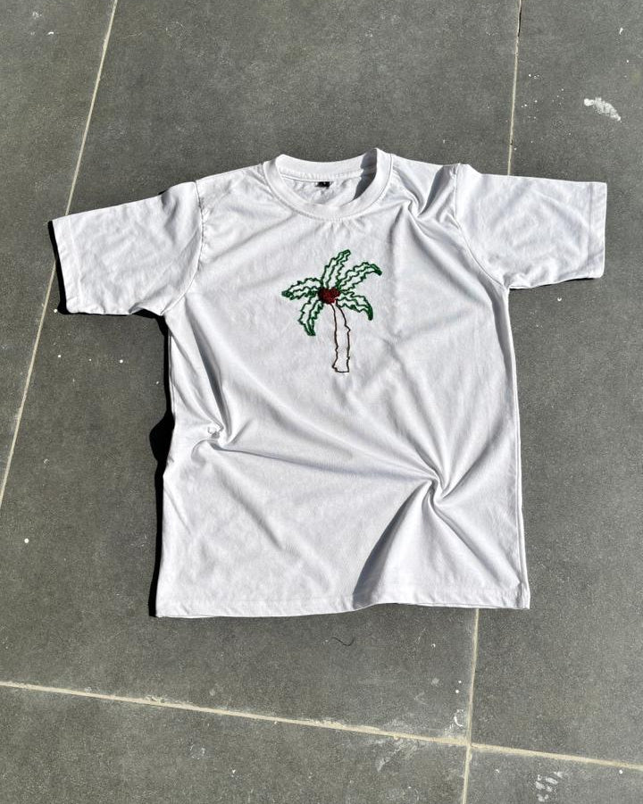 White t-shirt with a palm tree design bead embroidered on a gray tiled floor