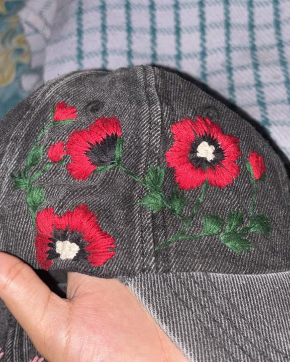 Gray cap with red floral embroidery held by a hand against a patterned fabric background