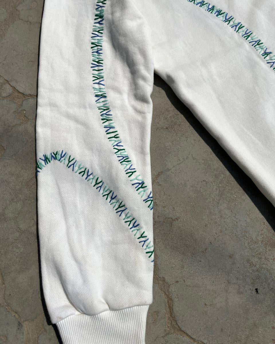 White sweatshirt with green stitching on a concrete floor