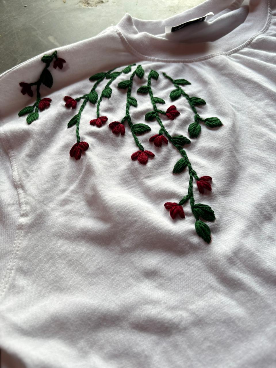 White shirt with red and green floral embroidery on a light background