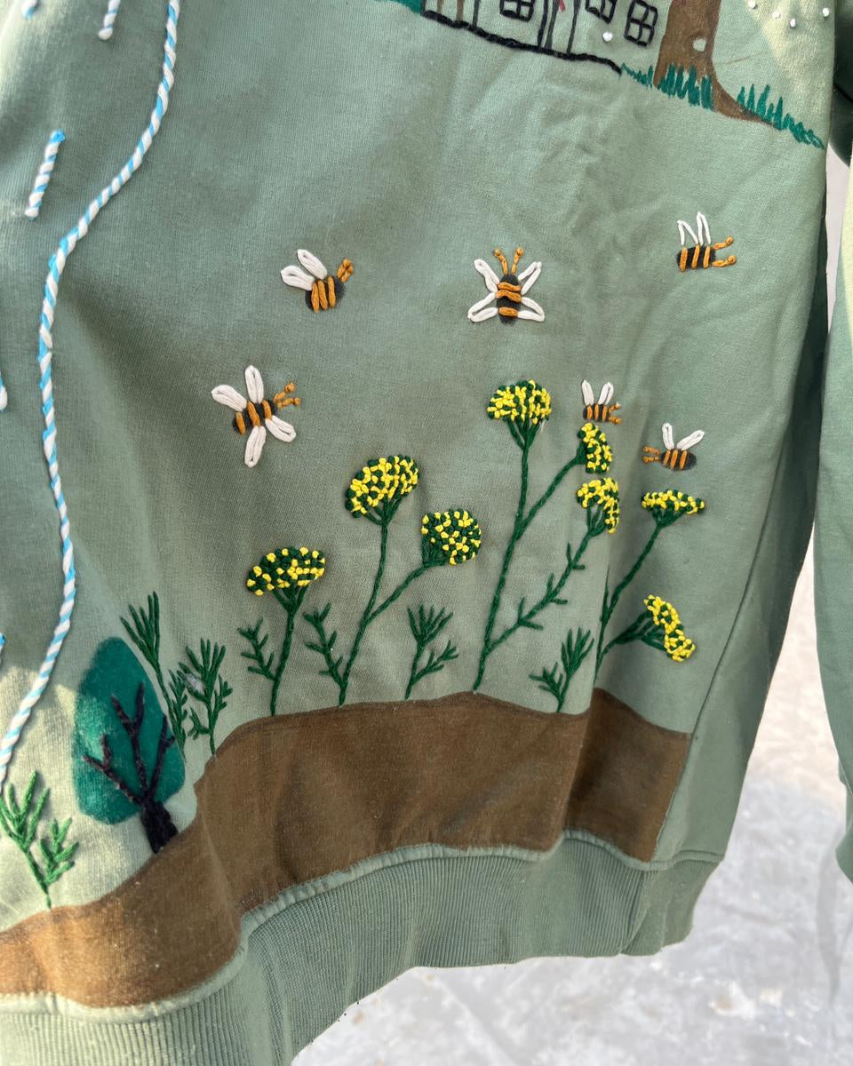 Embroidered fabric with bees, flowers, and trees on a green background