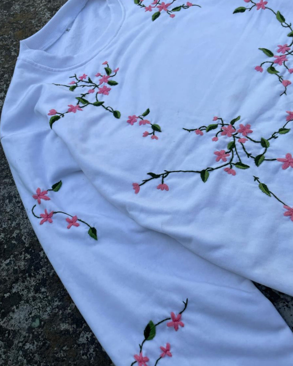 White long-sleeve shirt with floral embroidery on a textured surface