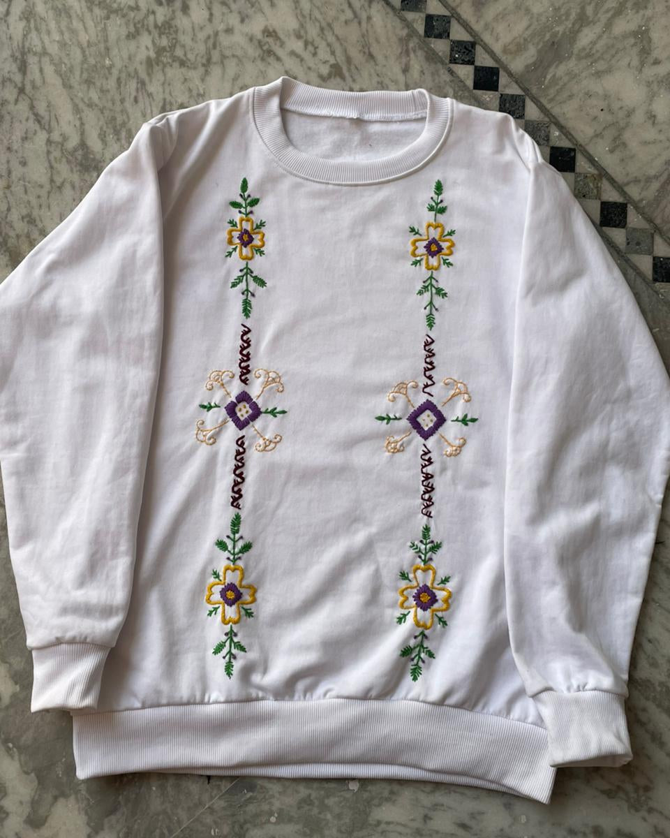 White sweatshirt with floral embroidery on a patterned surface