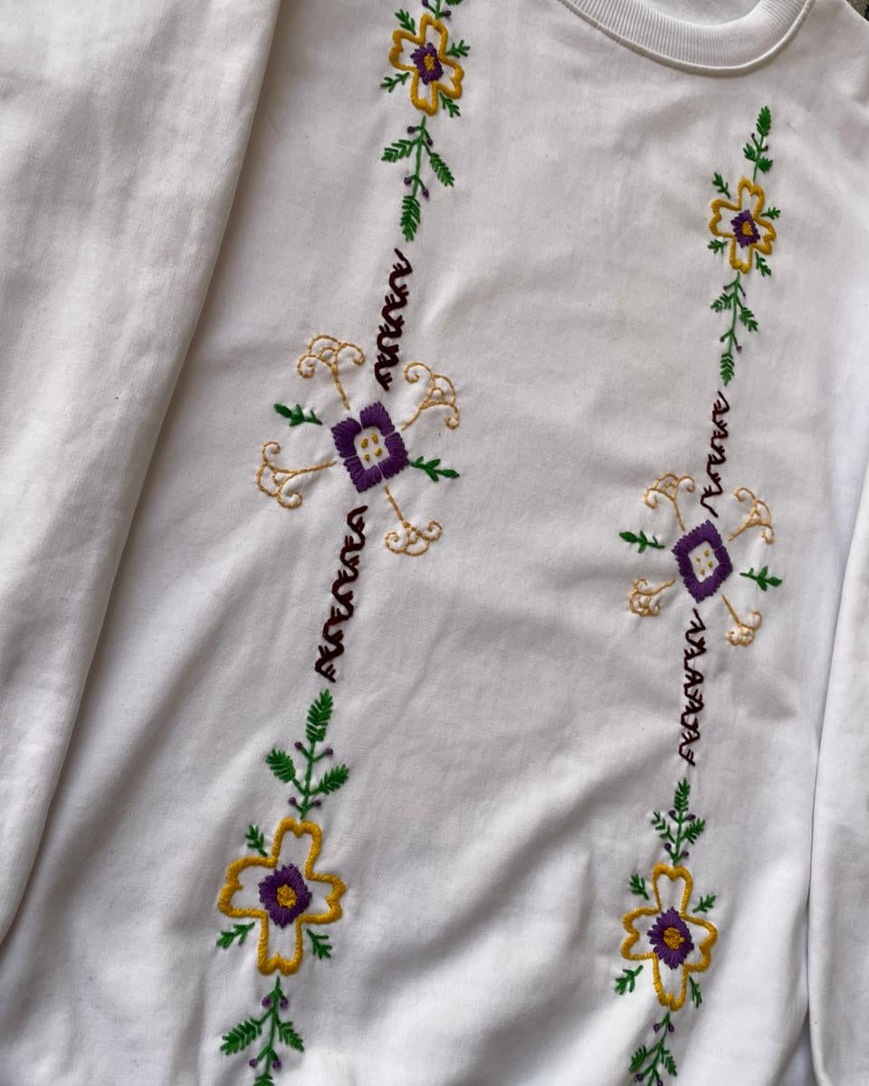 White sweatshirt with embroidered floral designs on a plain background