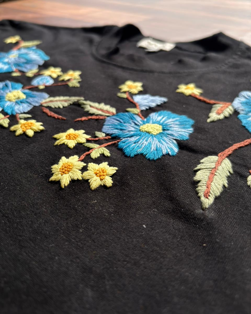 Black tshirt with colorful floral embroidery on a wooden surface