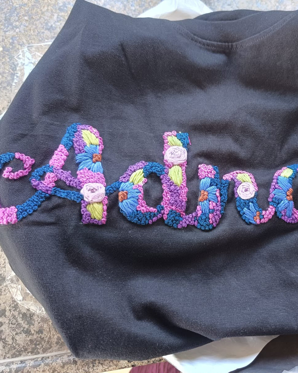 Black sweatshirt with colorful custom embroidered name 'Adrian' on a textured surface