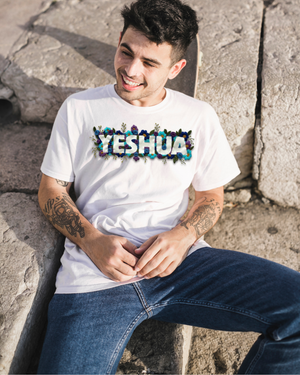 Person wearing a white t-shirt with 'YESHUA' name printed on it, sitting on stone steps.