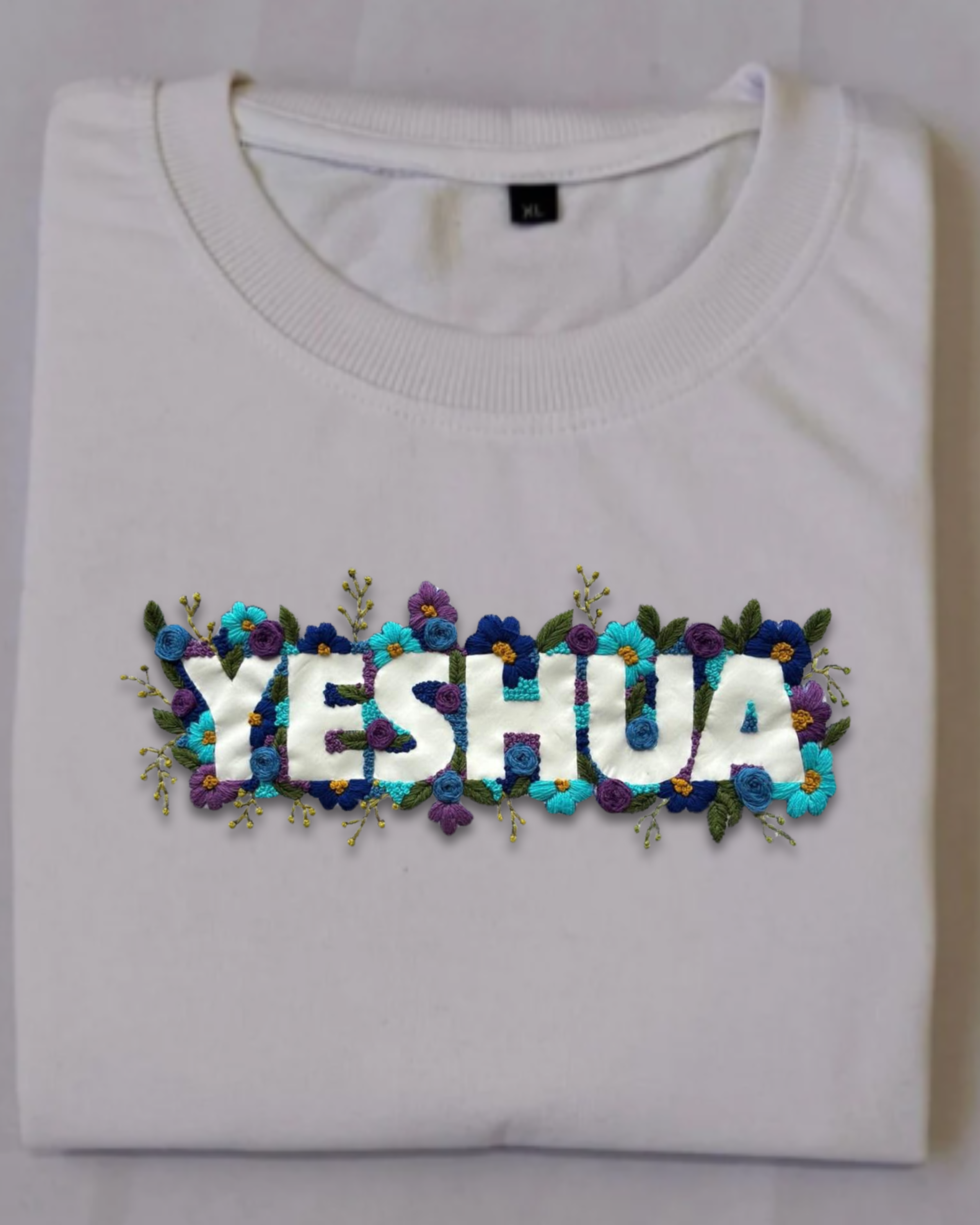 White sweatshirt with 'YESHUA' embroidered with flowers on a white background