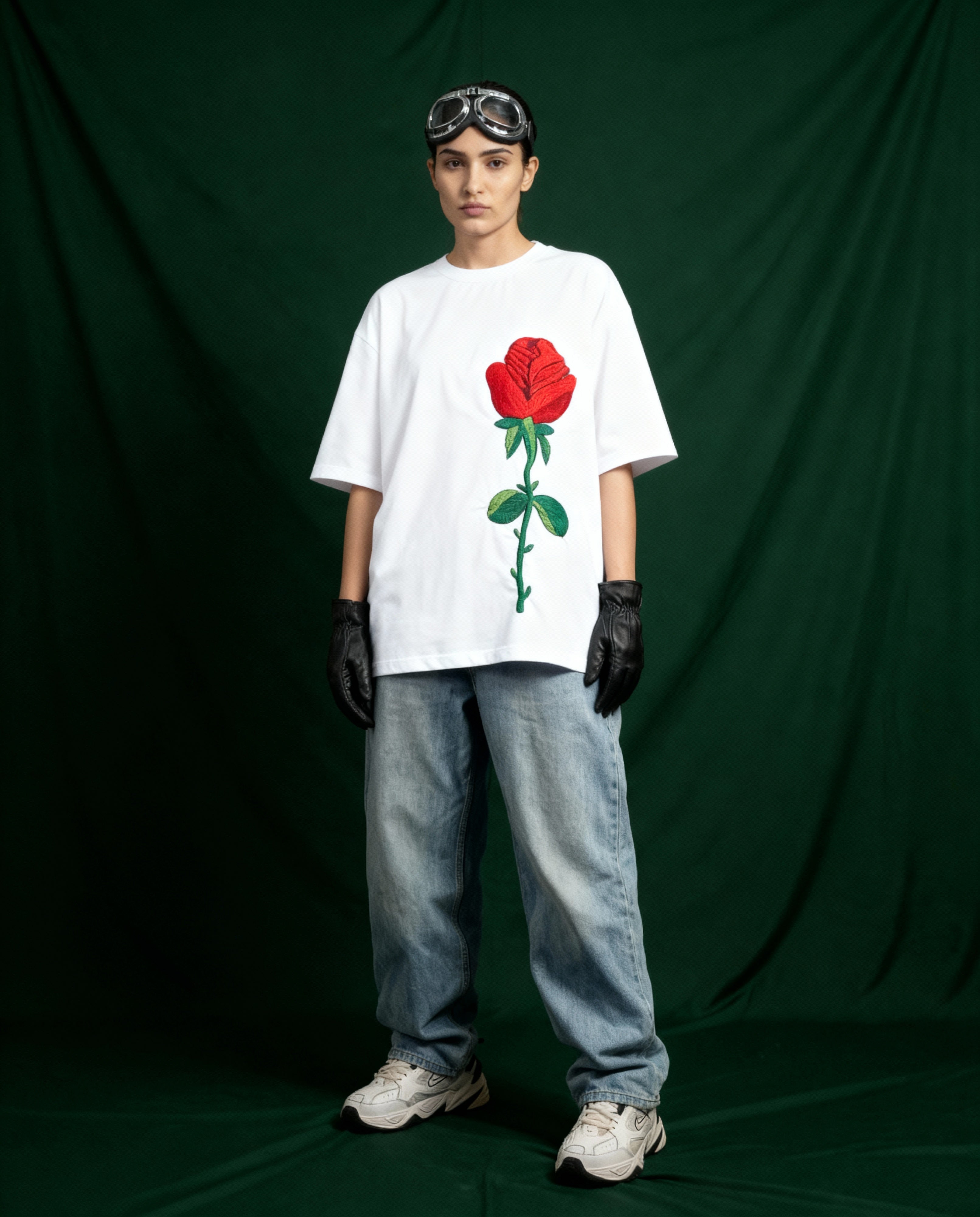 Person wearing a white t-shirt with a red rose graphic, standing against a dark green curtain.