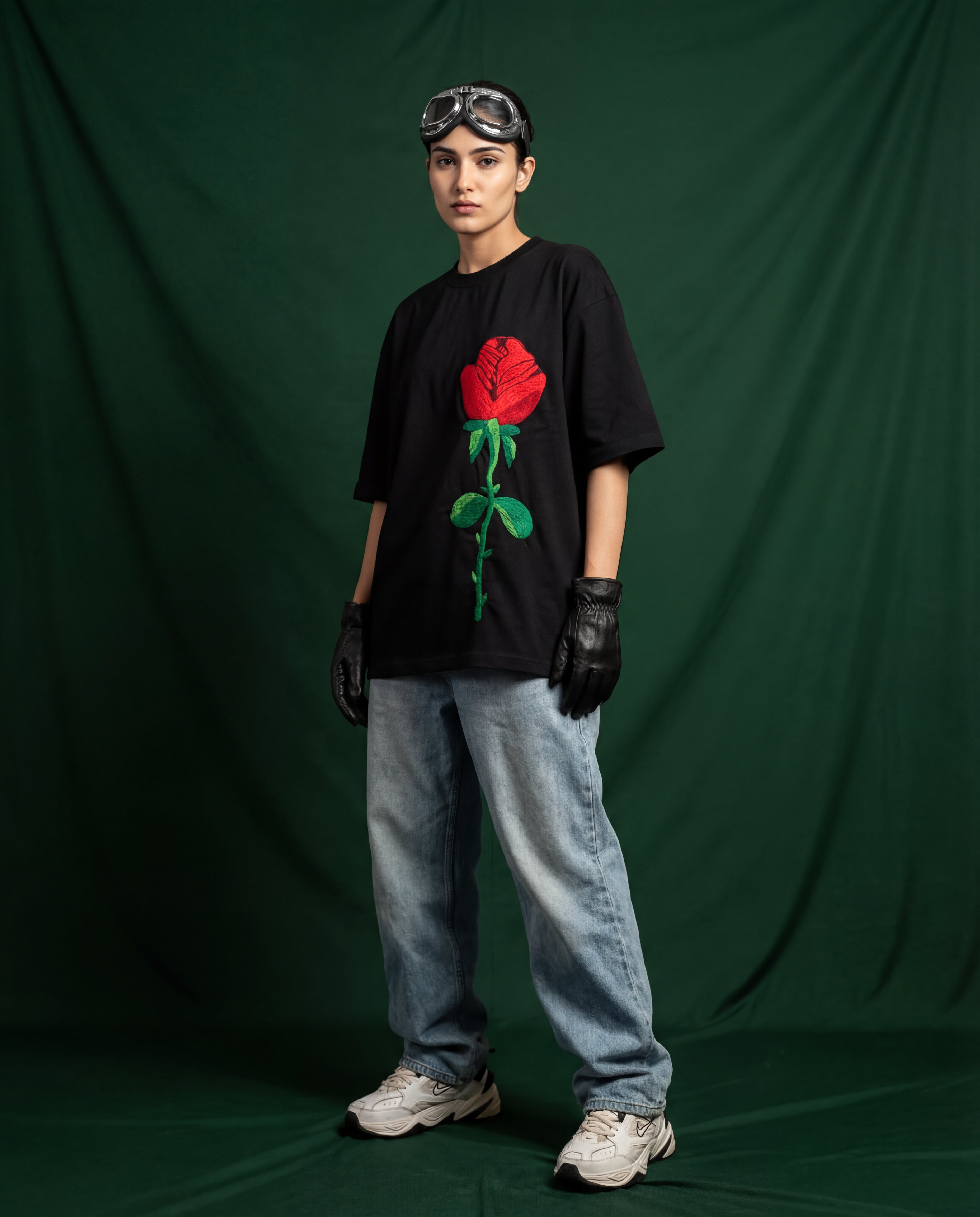 Person wearing a black t-shirt with a red rose embroidered design, standing against a green backdrop.