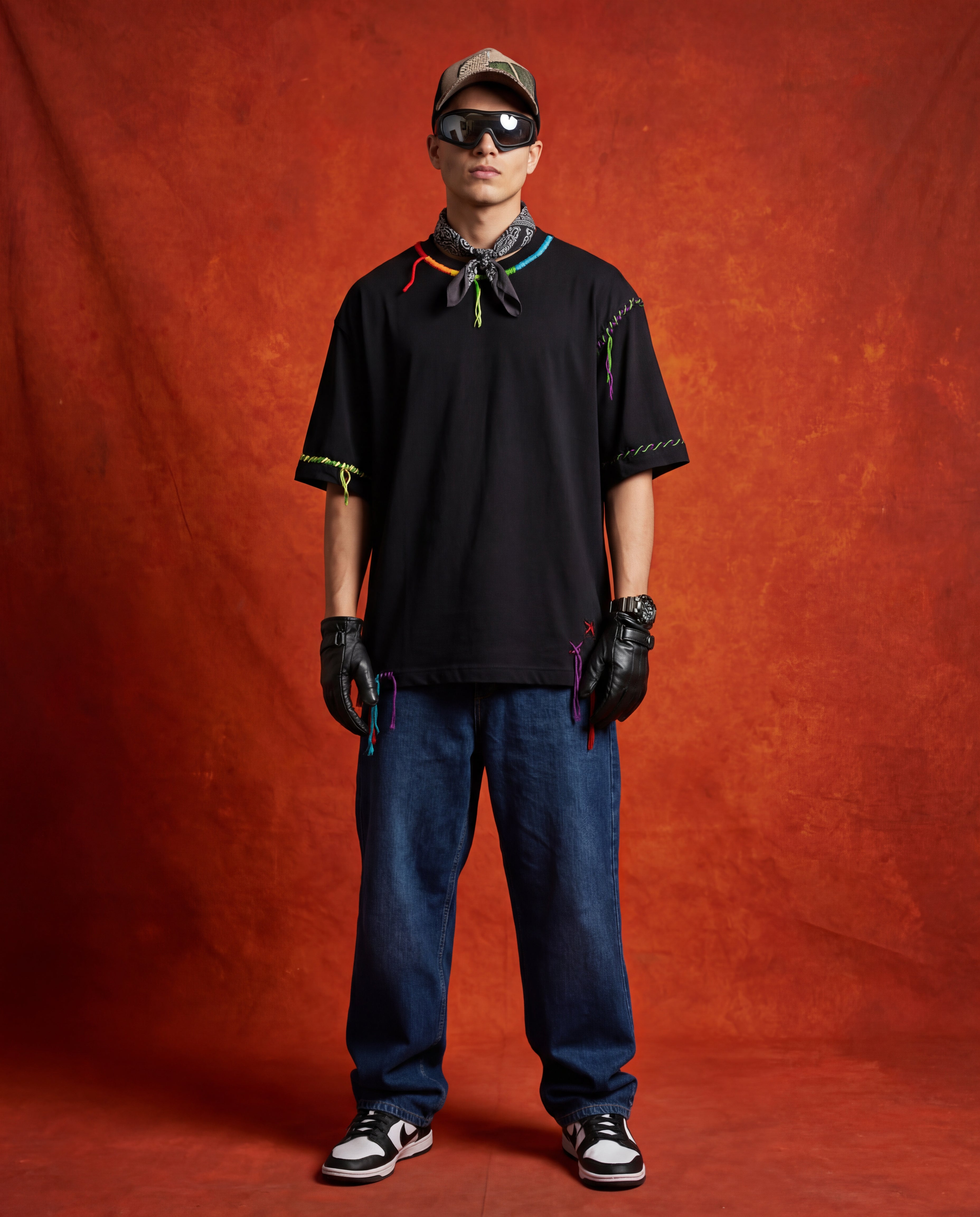 Person wearing a embroidered black t-shirt, blue jeans, and black gloves against a red background